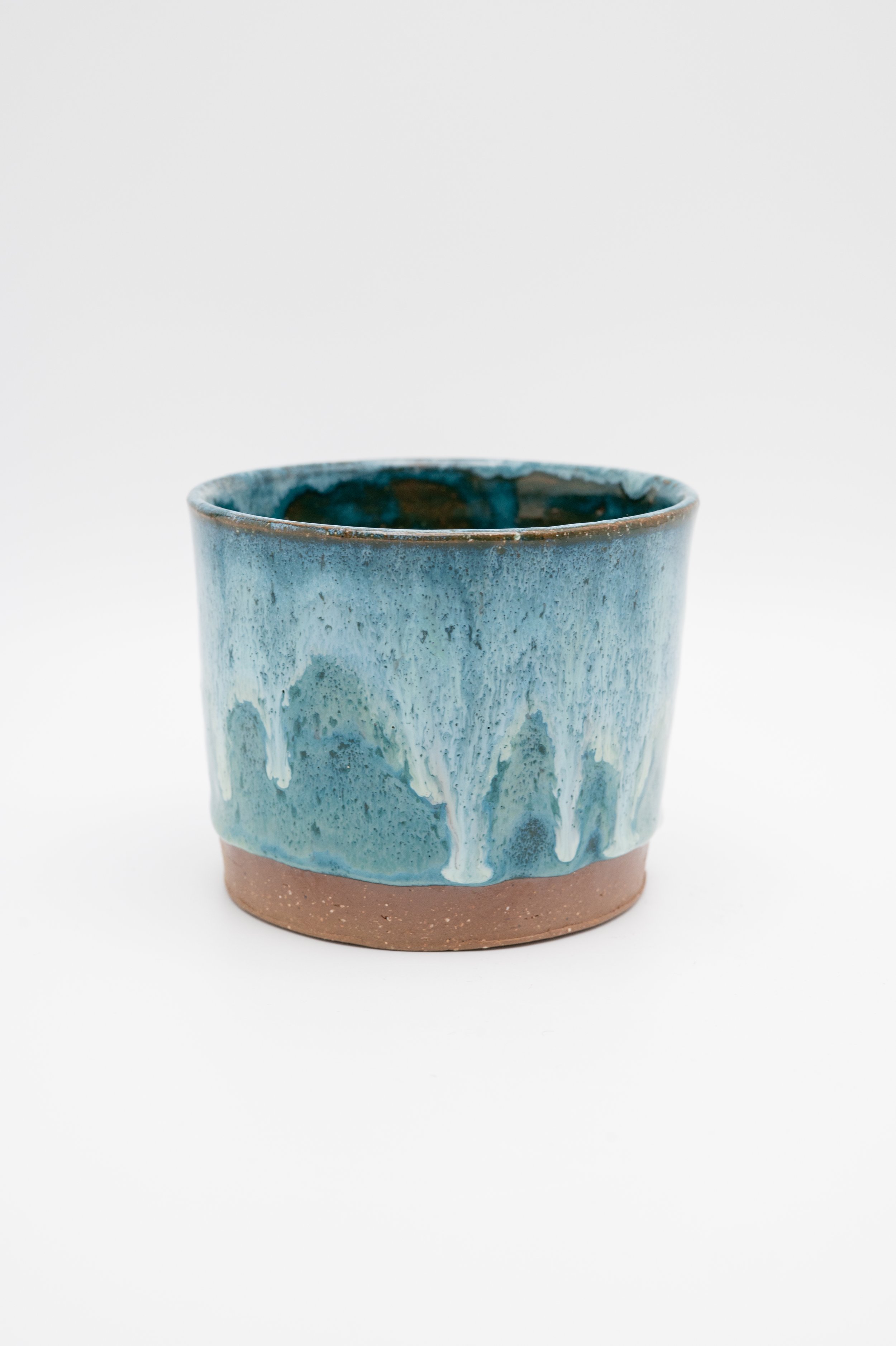 A ceramic pot with a brown base and a blue glaze with white drips running down its sides, set against a plain white background.
