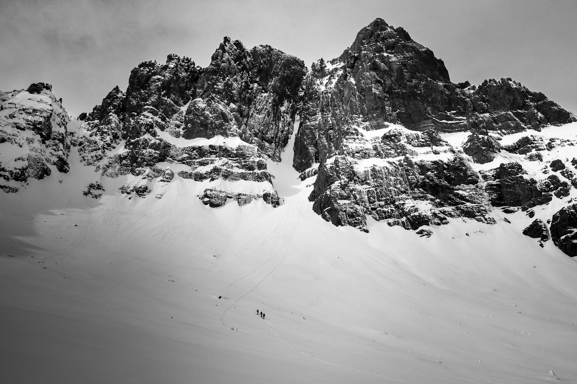 Snow-covered mountain with a steep slope and a few small human figures at the bottom. Yellowstone National Park