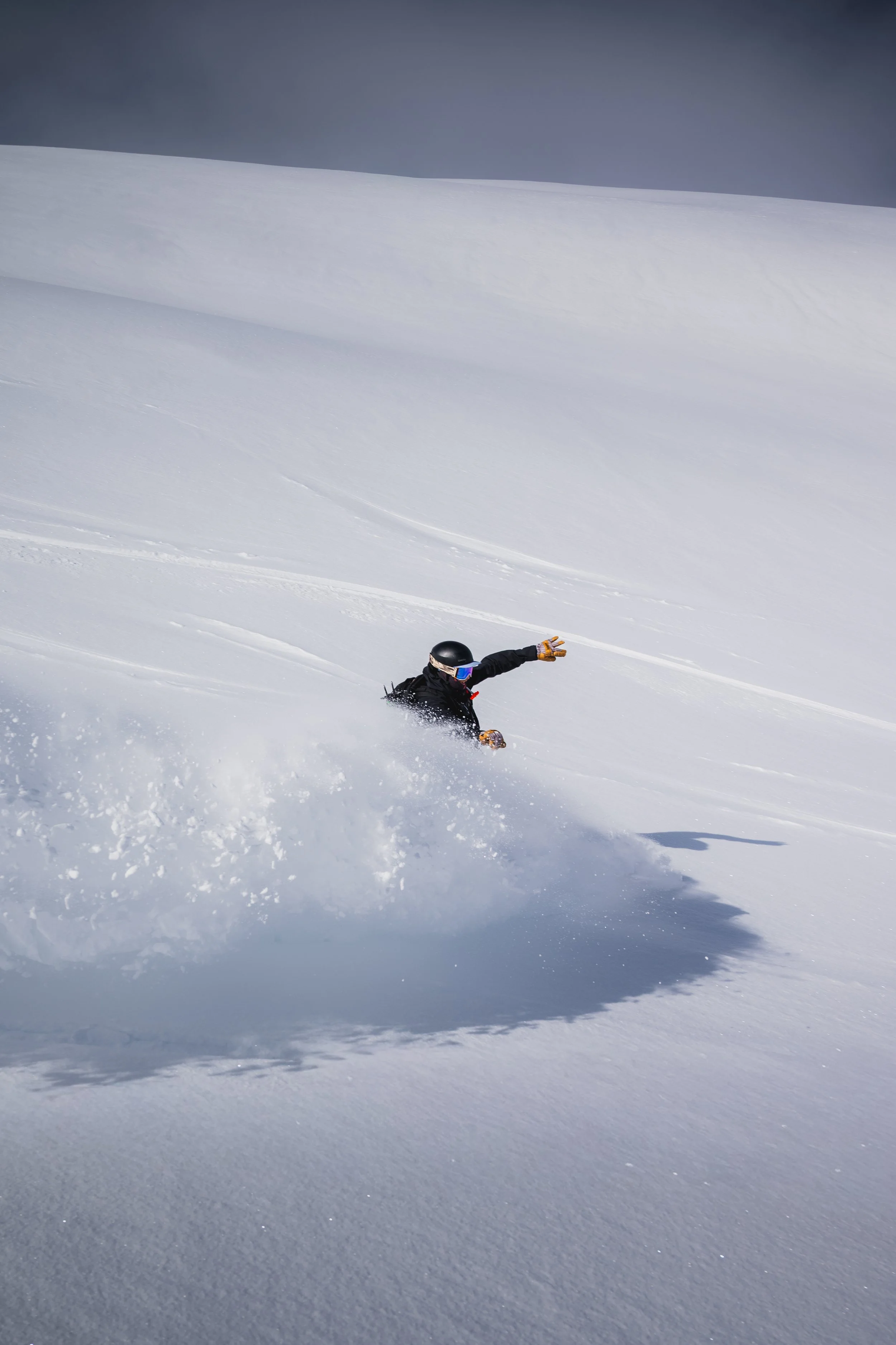 Person in winter gear snowboarding or skiing down a snowy slope in a mountainous area.