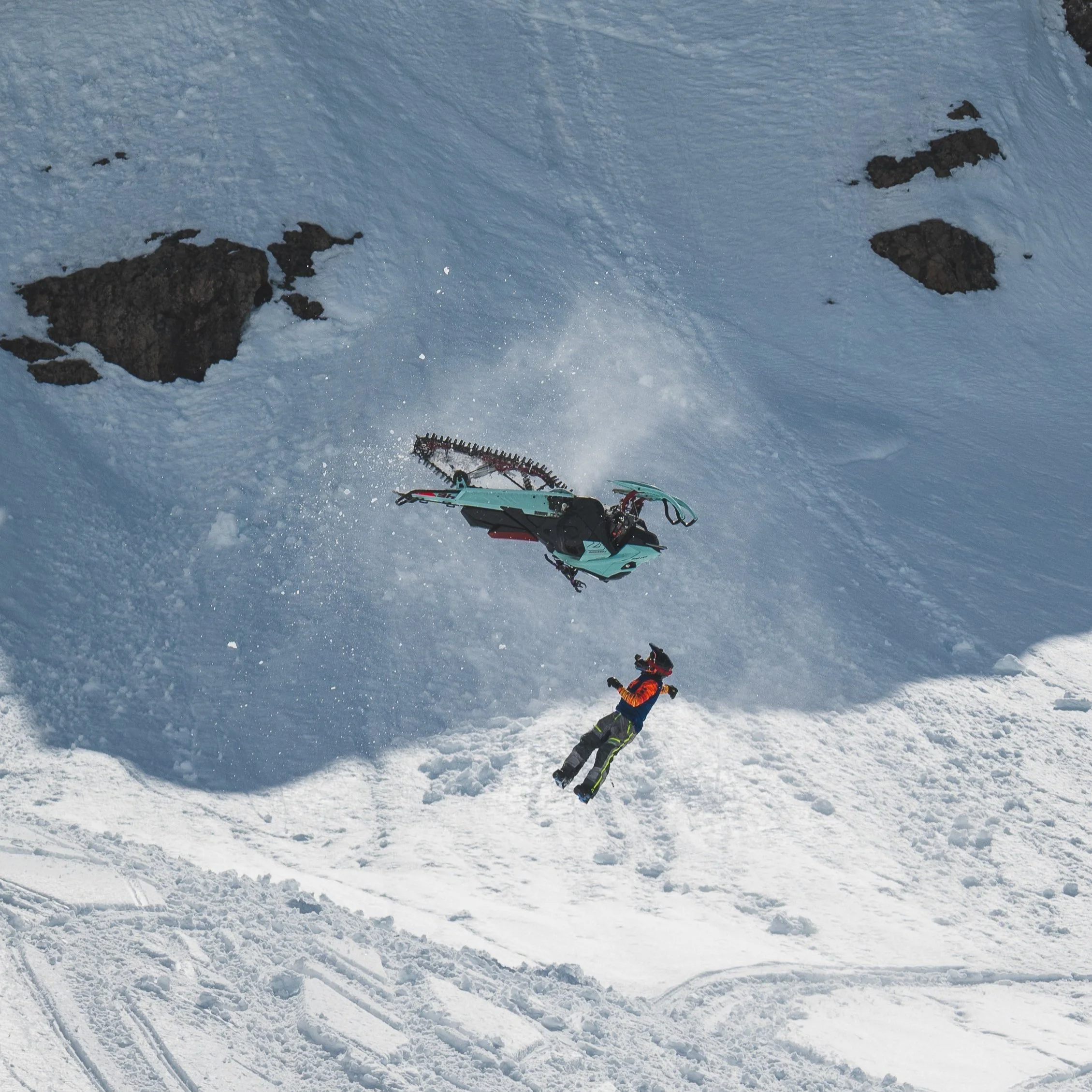 A person falling off a snowmobile on a snowy mountain slope.