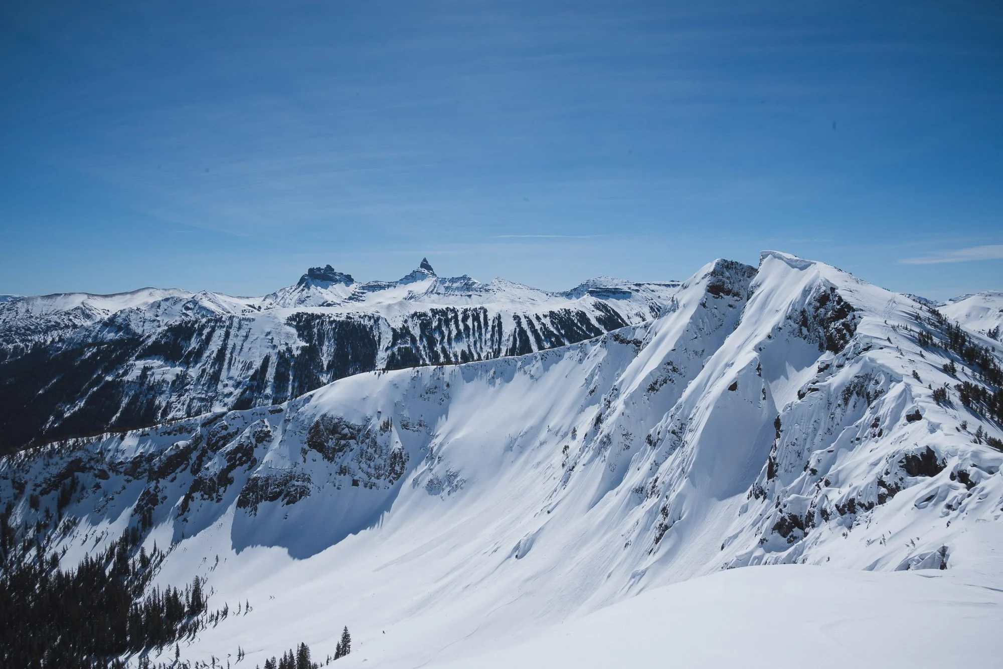 Snow-covered mountain range under a clear blue sky with prominent peaks. Montana Backcountry skiing
