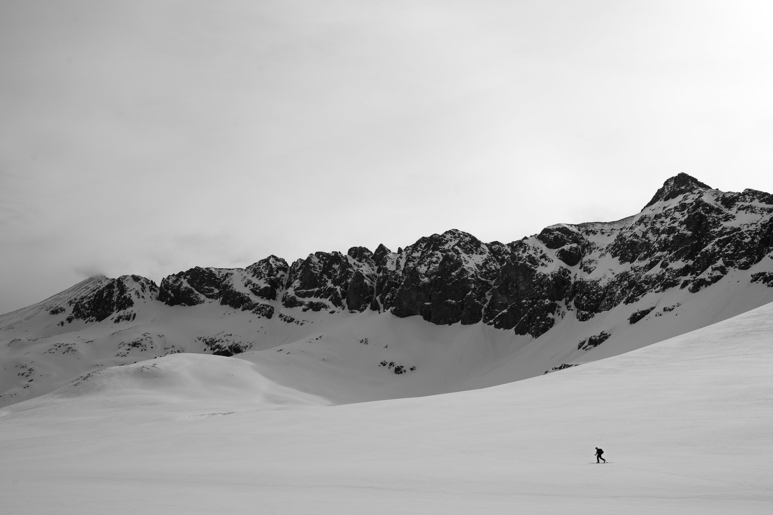 A person skiing on a snowy landscape with rugged mountain peaks in the background in black and white.