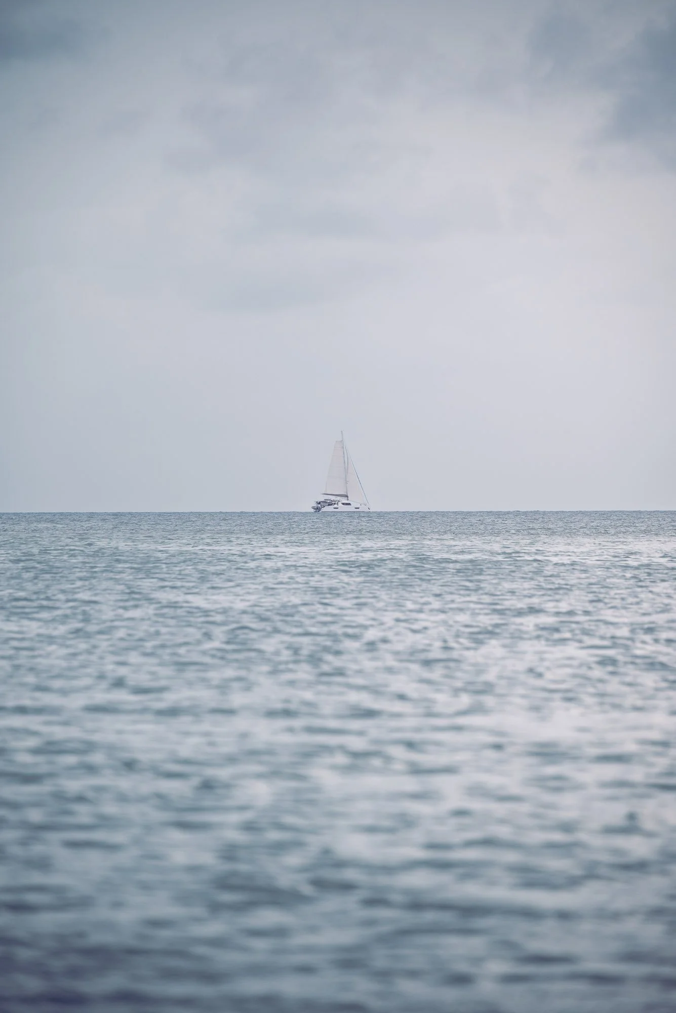 A sailboat on the horizon in a calm sea with a cloudy sky above. Turneffe Flats, Belize