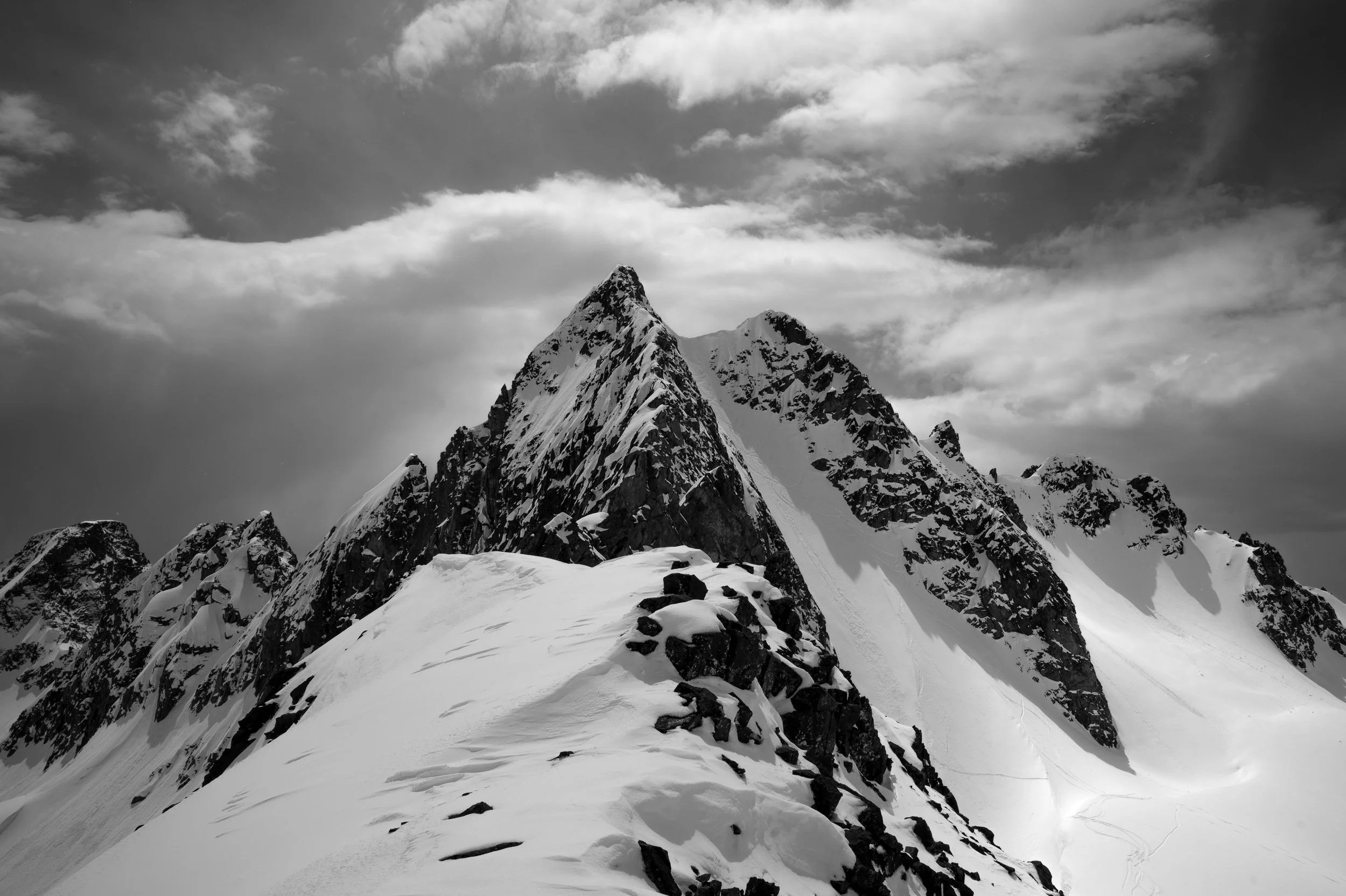 Snow-covered mountain peaks under a cloudy sky in black and white.