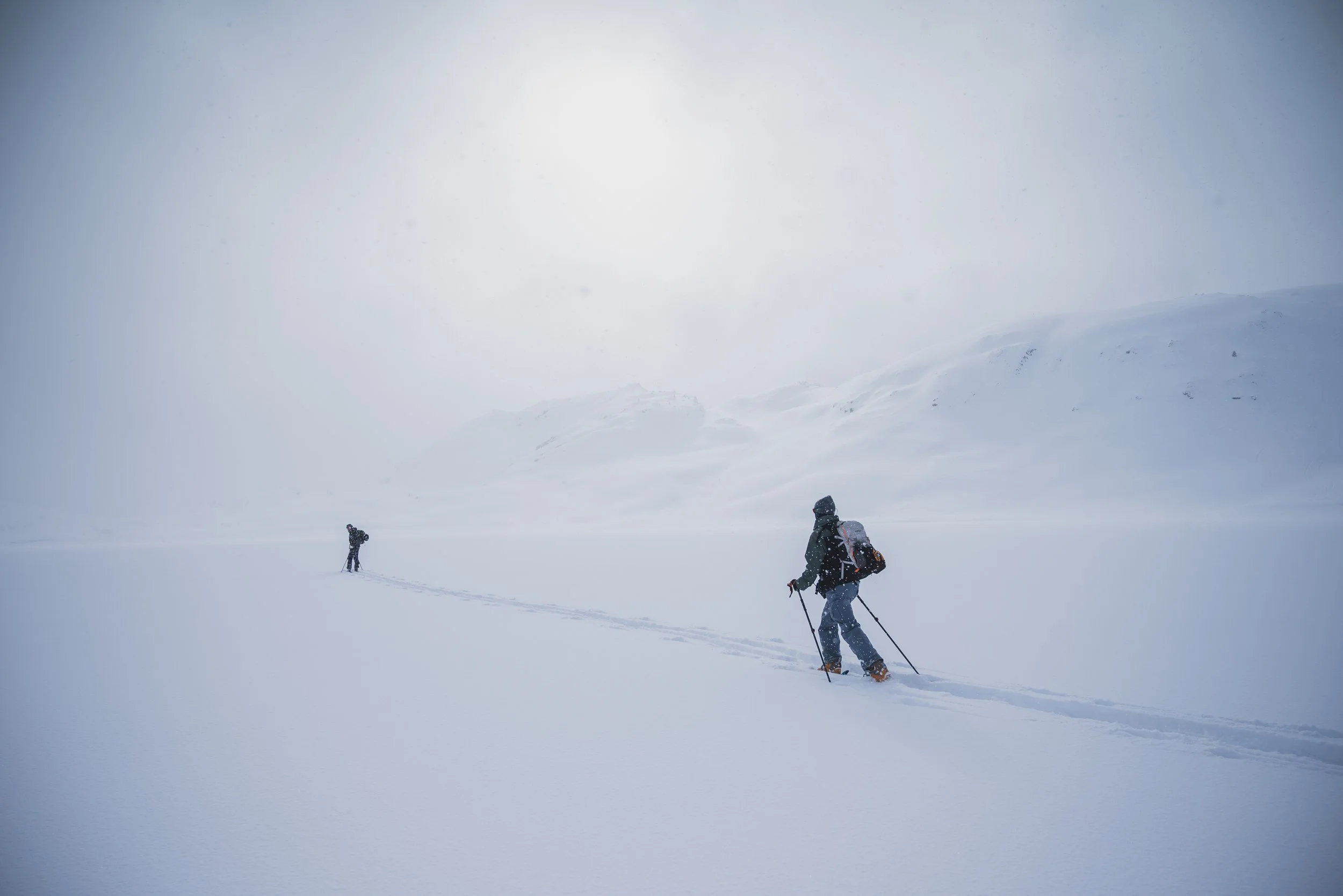 Two people cross-country skiing on a snowy, foggy landscape with distant hills and low visibility.