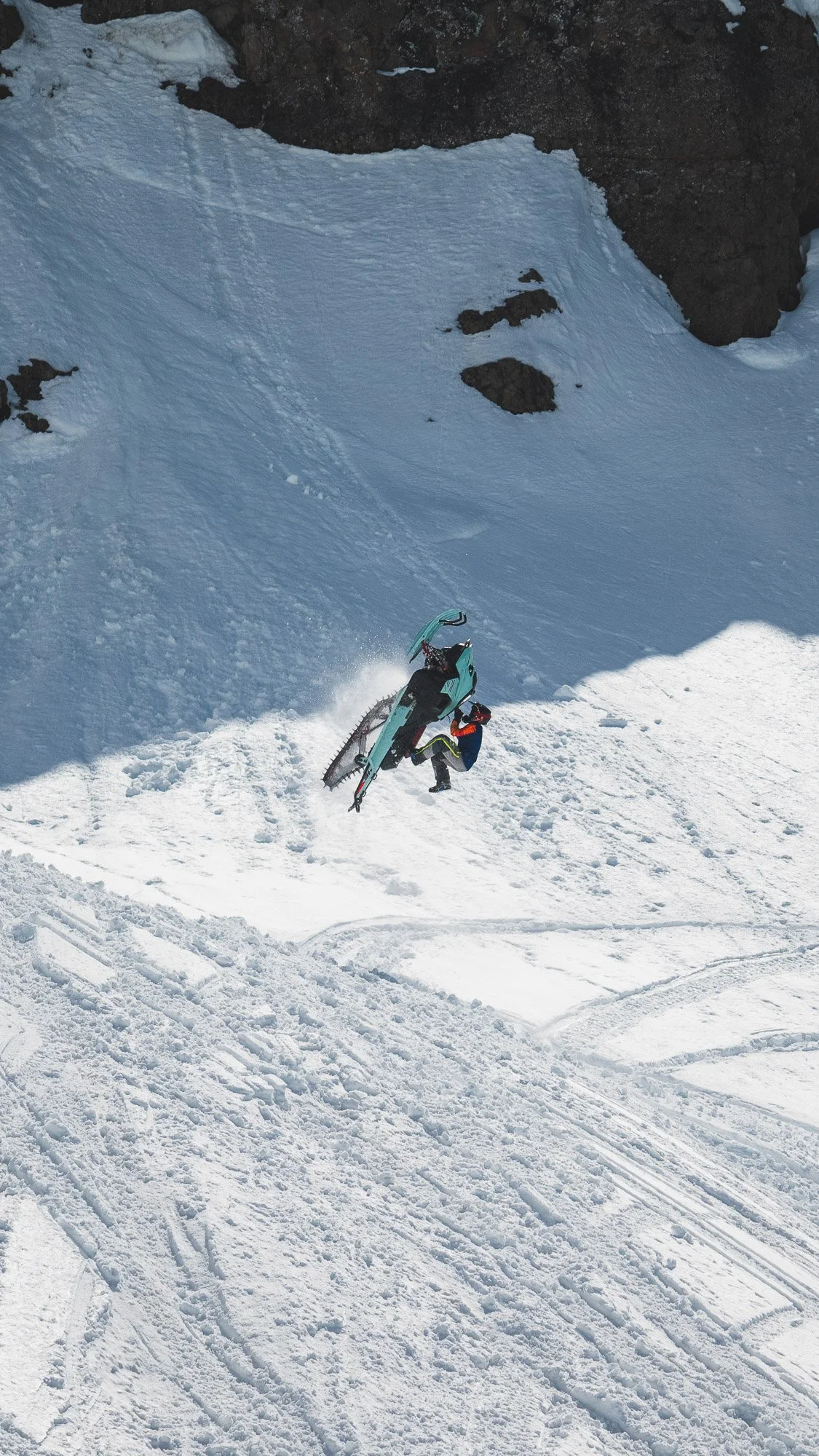 A person falling while riding an alpaca snowmobile down a snowy mountain slope. Montana backcountry snowmobiling
