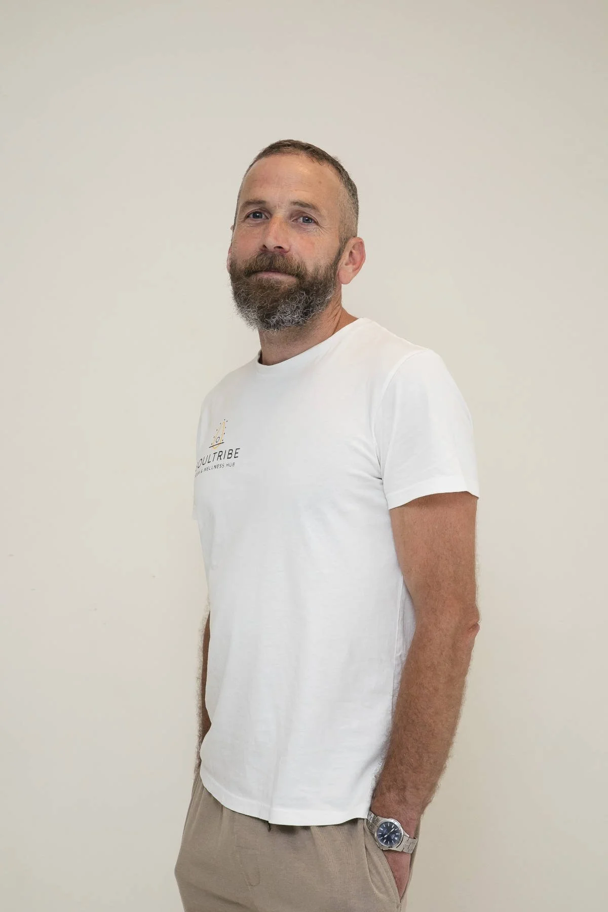 Man in black tank top seated cross-legged on a yoga mat in a room with light-colored walls.