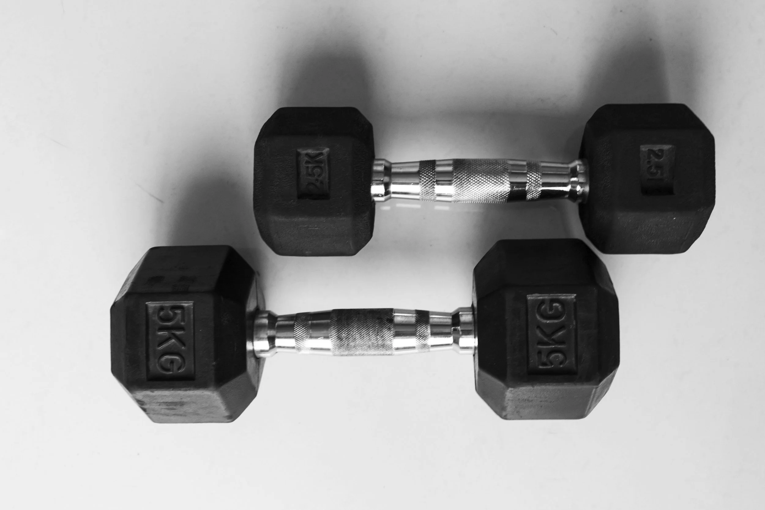 Pair of black 5-kilogram dumbbells with textured silver handles on a white surface.