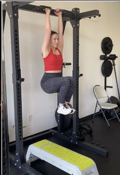 A woman performing hanging knee raises for core strength on a pull-up rig at 901FitLife, a functional fitness gym in Memphis.