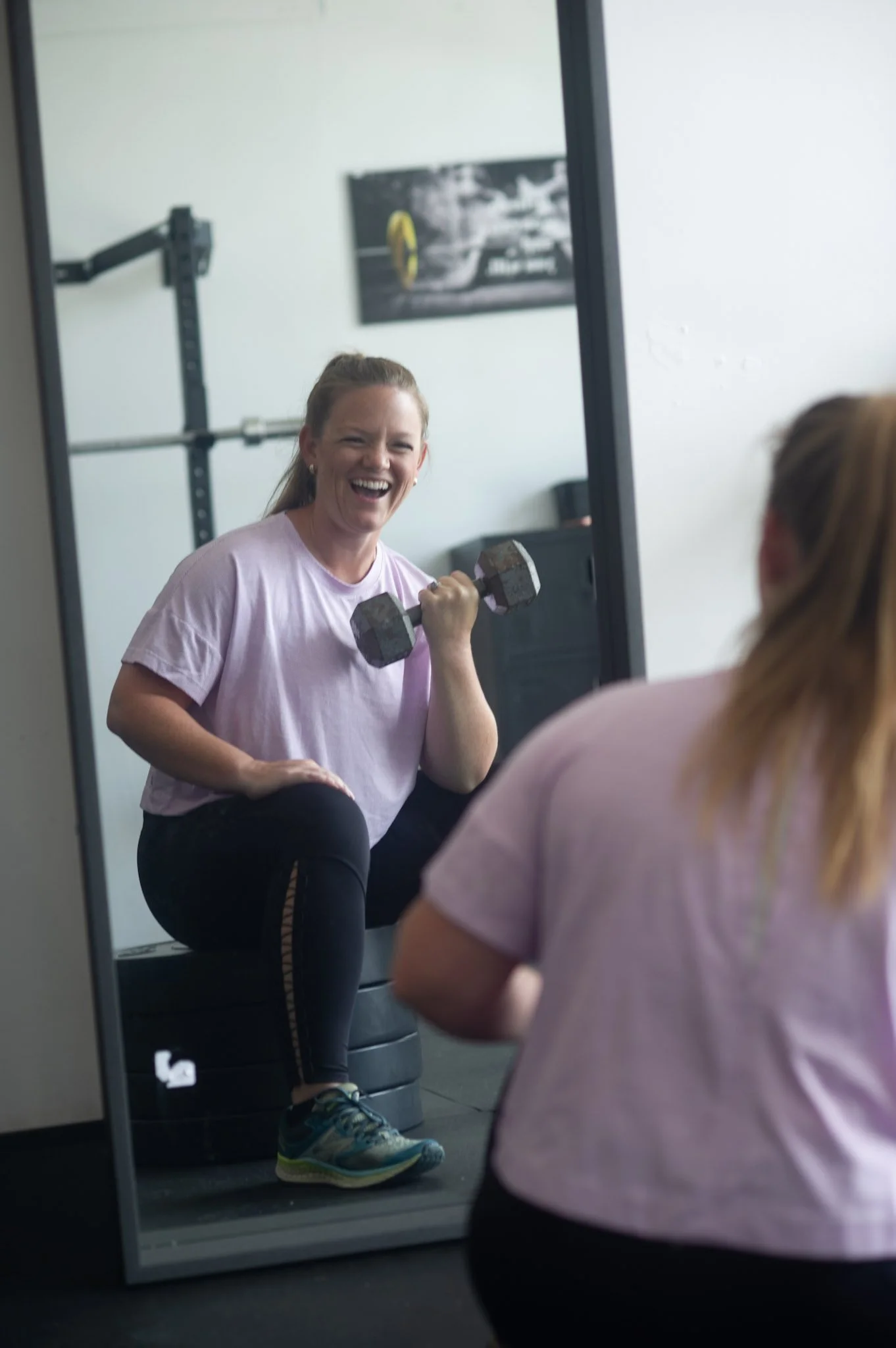 A smiling woman performing a dumbbell bicep curl while looking in the mirror at 901fitlife, focusing on personal strength and fitness goals in Memphis