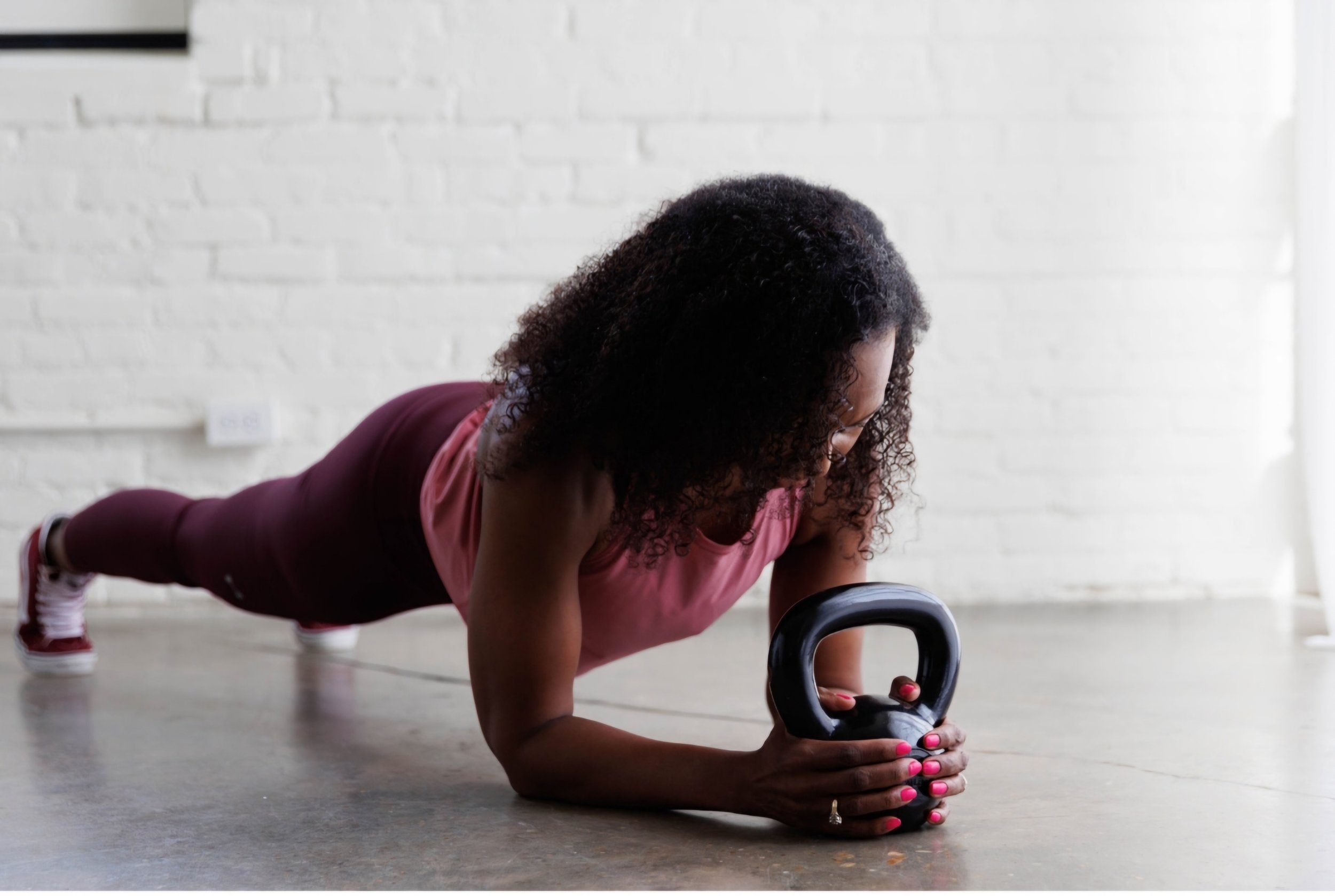 A woman performing a core-strengthening kettlebell plank against a white brick wall at 901FitLife, a functional fitness studio in Memphis.