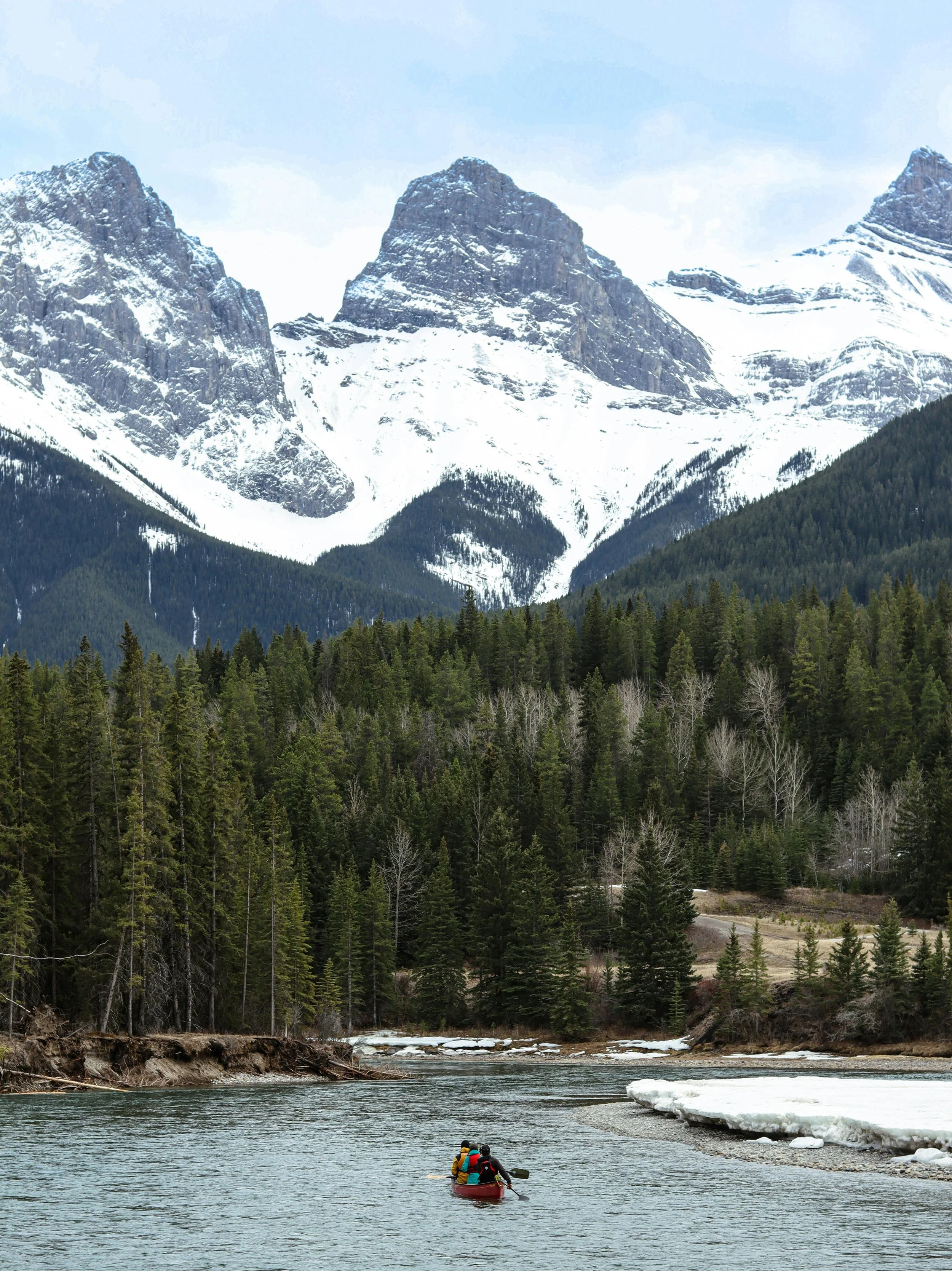 people paddling down cold river towards snowy mountain backdrop
