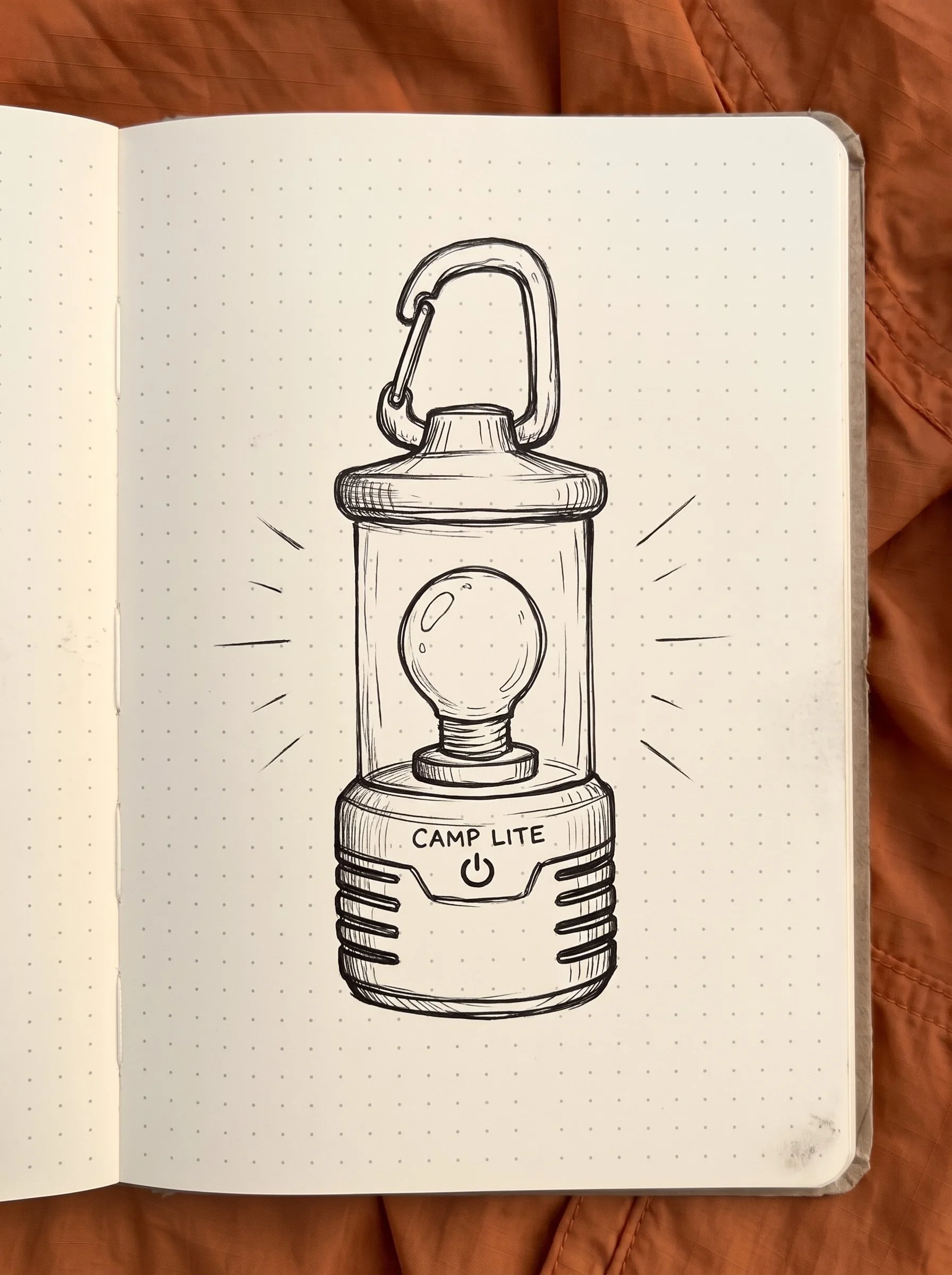 Hand-drawn illustration of a fictional Camp Lite camping lantern in an open field notebook.
