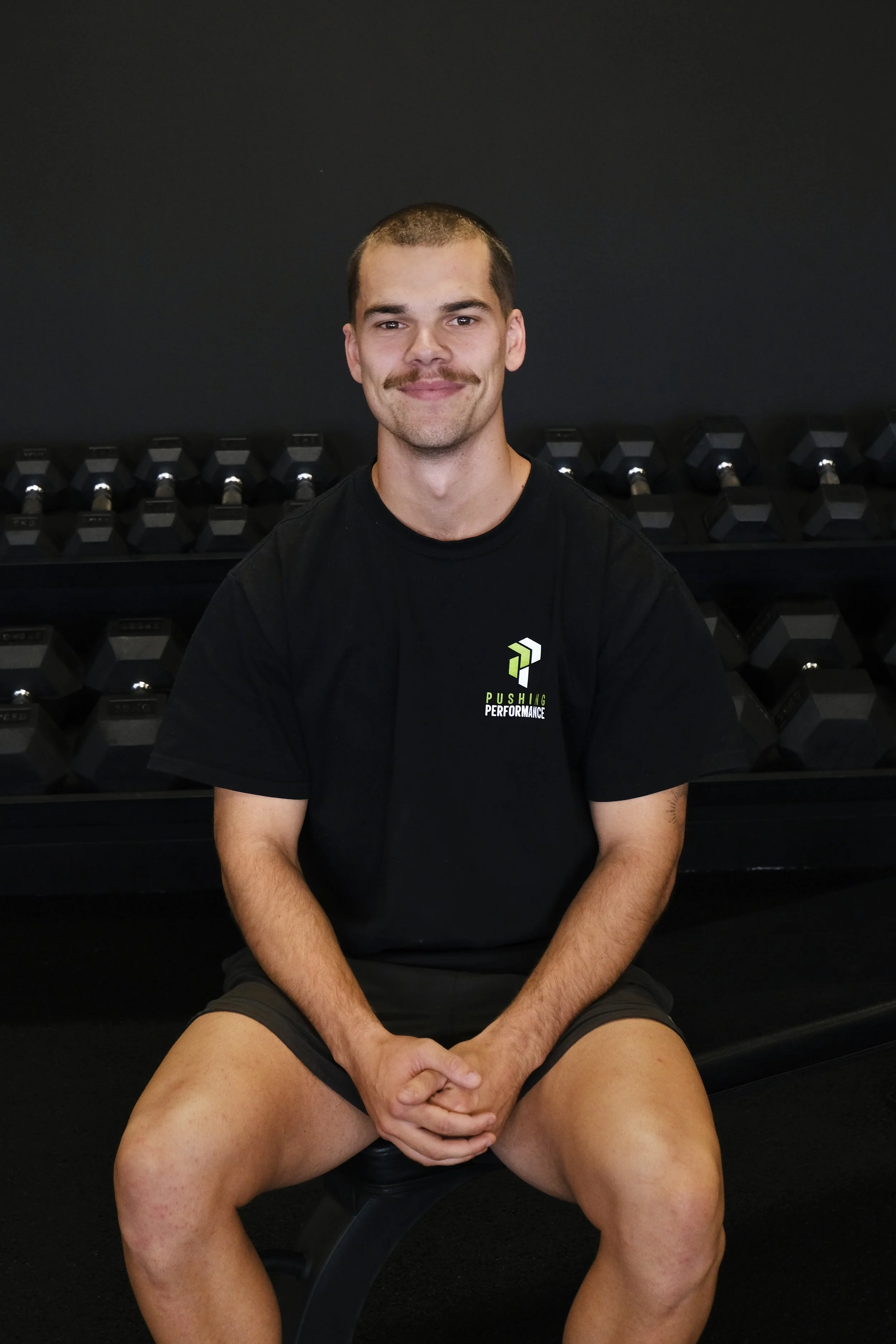 Man sitting on a bench in a gym with dumbbells in the background.