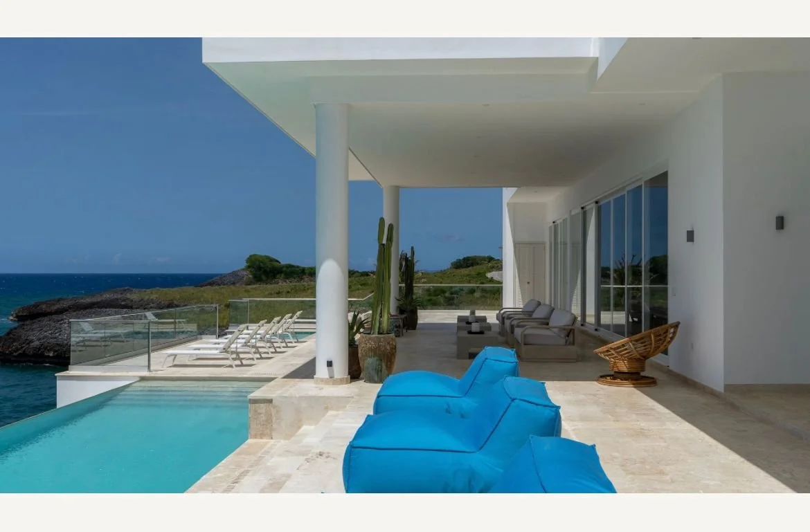 Terraza moderna con piscina, sillones azules, vista al mar y cactuses decorativos.