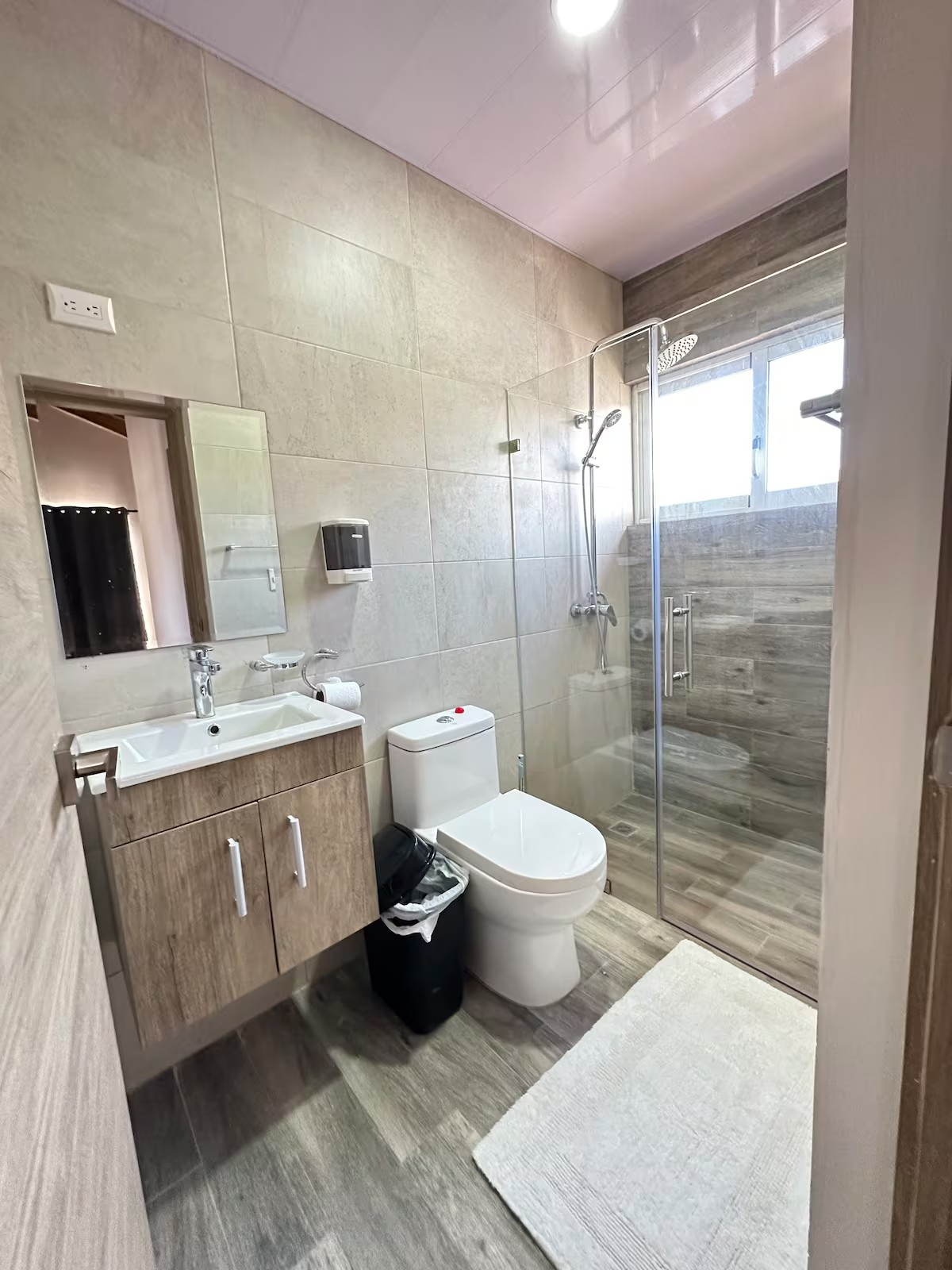 Modern bathroom with a glass shower, toilet, vanity with sink, mirror, and wall-mounted soap dispenser.