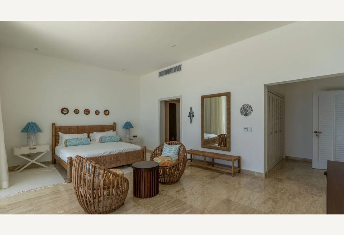 Habitación amplia con cama doble, lámparas azules, sillas de mimbre, mesa pequeña, espejo grande y decoración en las paredes.