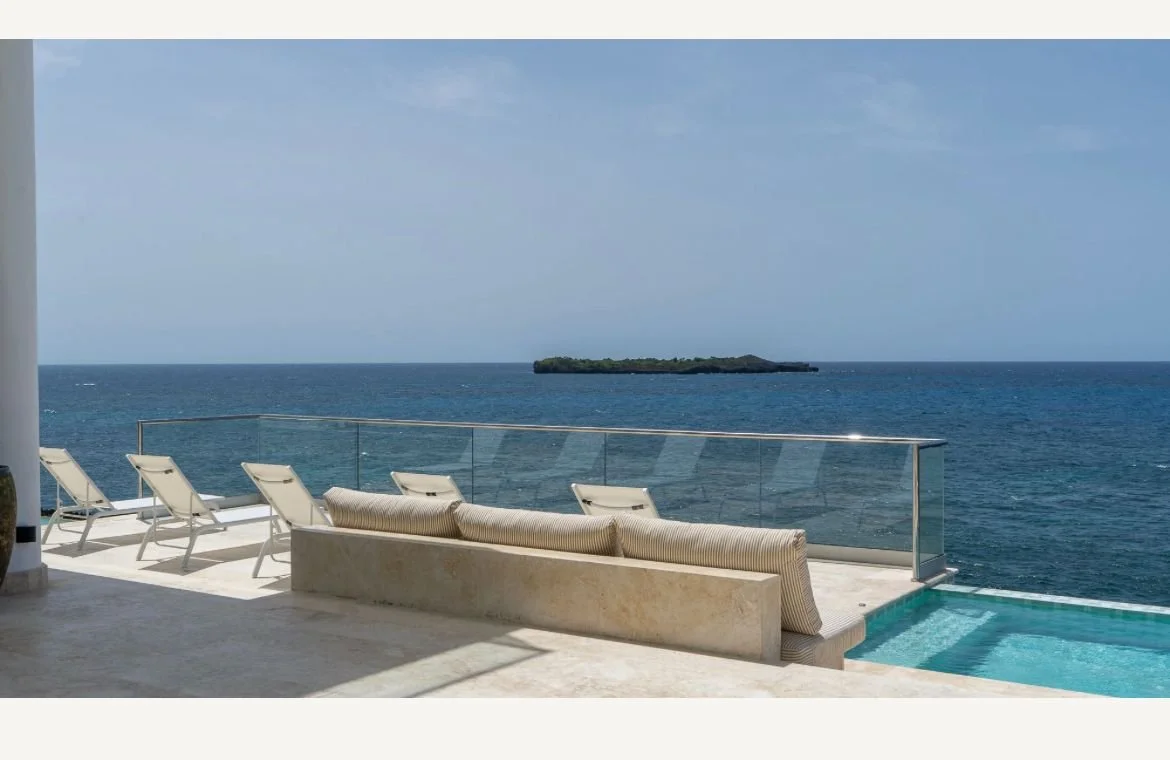 Terraza moderna con sillas reclinables, piscina y vista al océano.