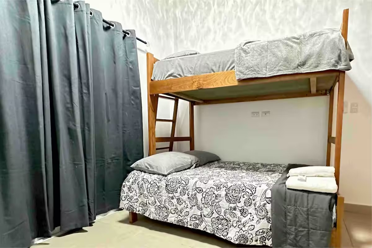 Bedroom with wooden bunk bed, floral-patterned bedding, gray curtains, and folded towels on the bottom bed.