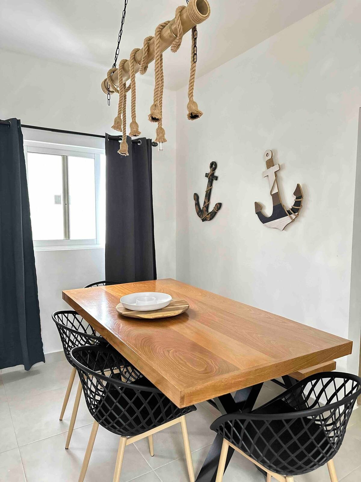 Dining room with a wooden table, four black chairs, nautical-themed wall decor, and rope light fixture.