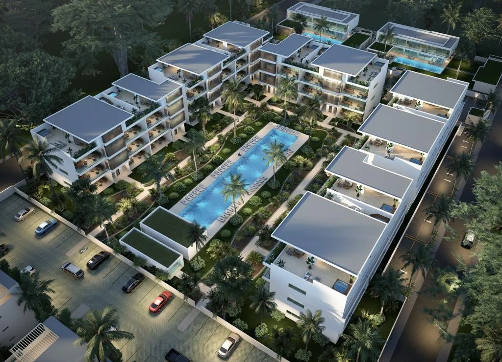 Vista aérea de un complejo residencial moderno con piscina central, rodeado de edificios de apartamentos y áreas verdes, iluminado por la noche.