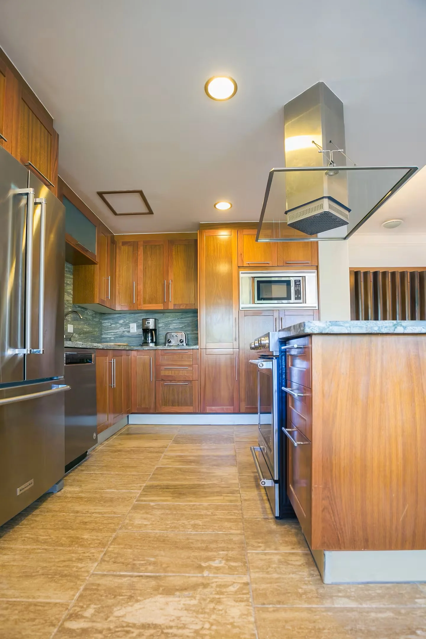 Cocina moderna con gabinetes de madera, electrodomésticos de acero inoxidable, encimera de granito y pisos de cerámica.