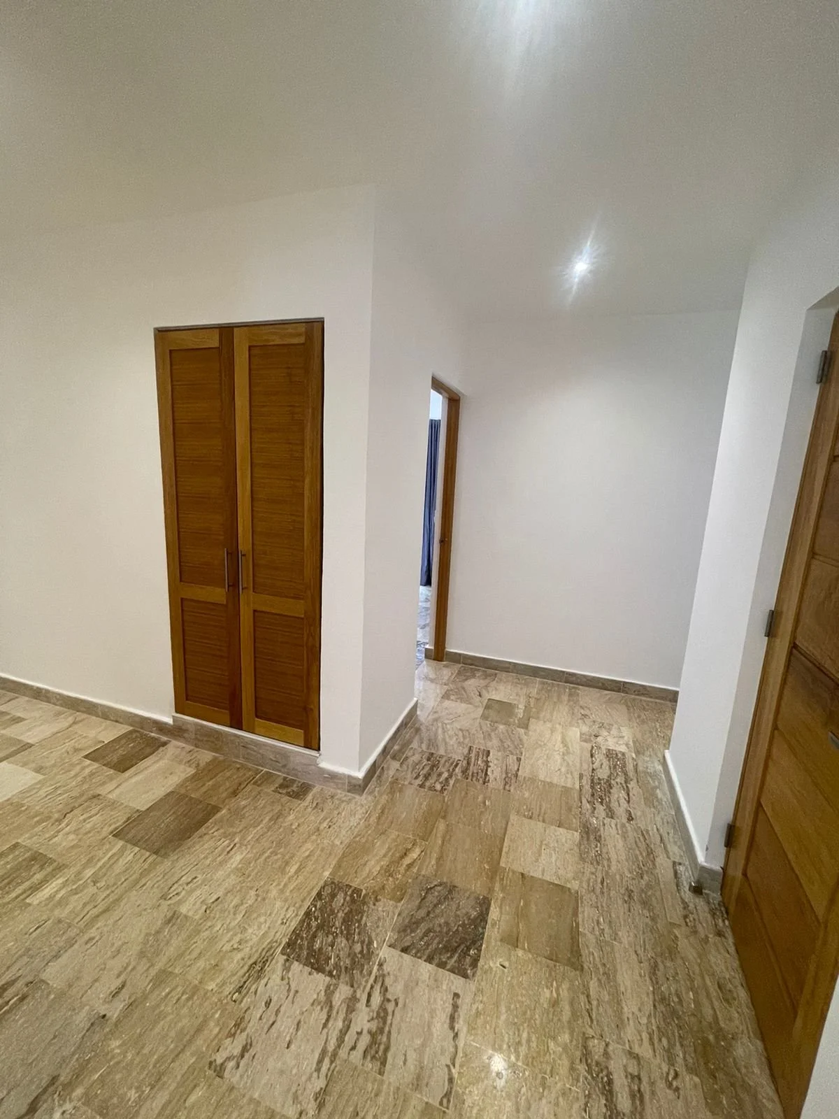 Interior hallway with light brown marble tile flooring, white walls, and wooden doors.