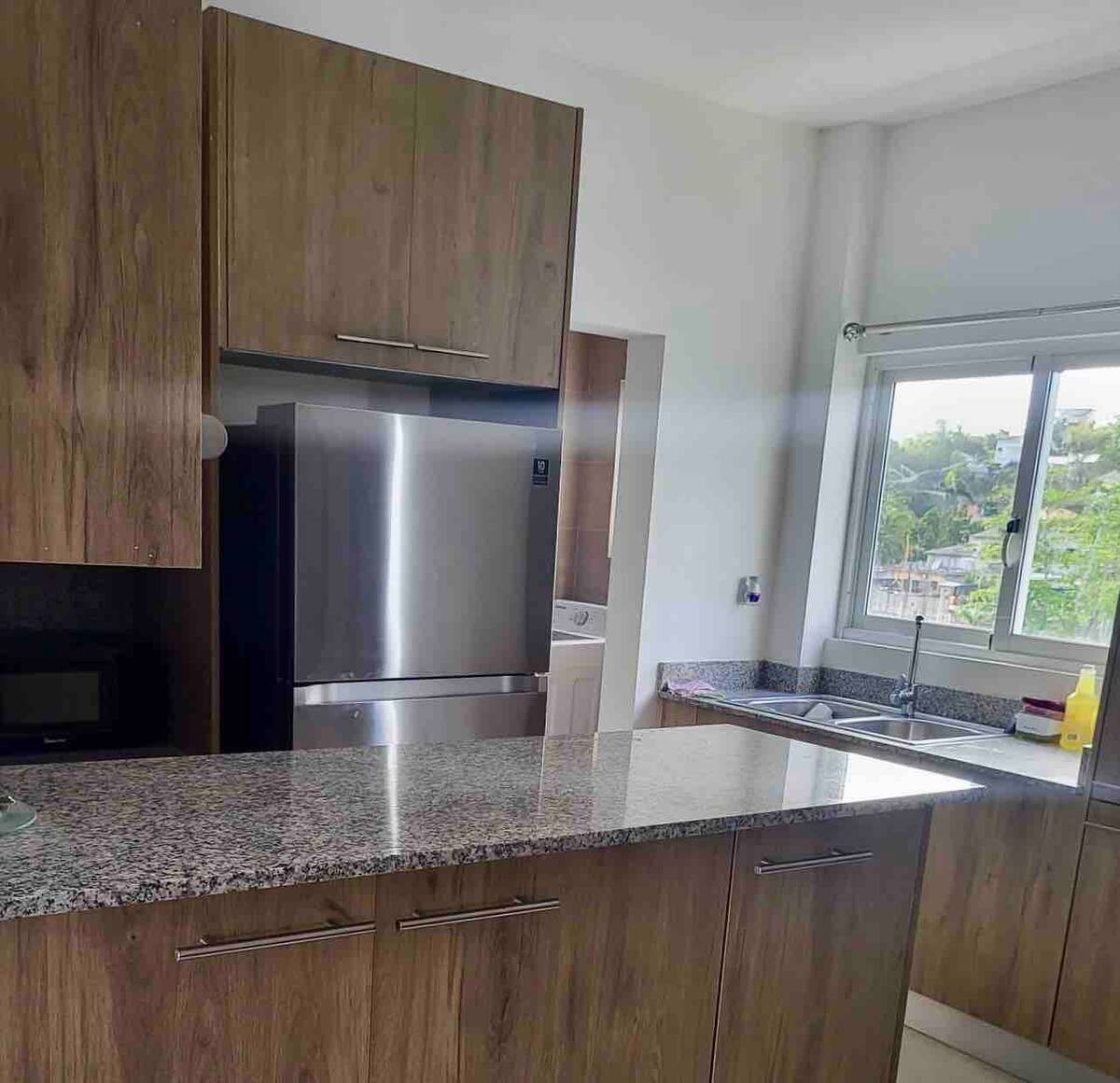 Modern kitchen with wooden cabinets, stainless steel refrigerator, and granite countertops.
