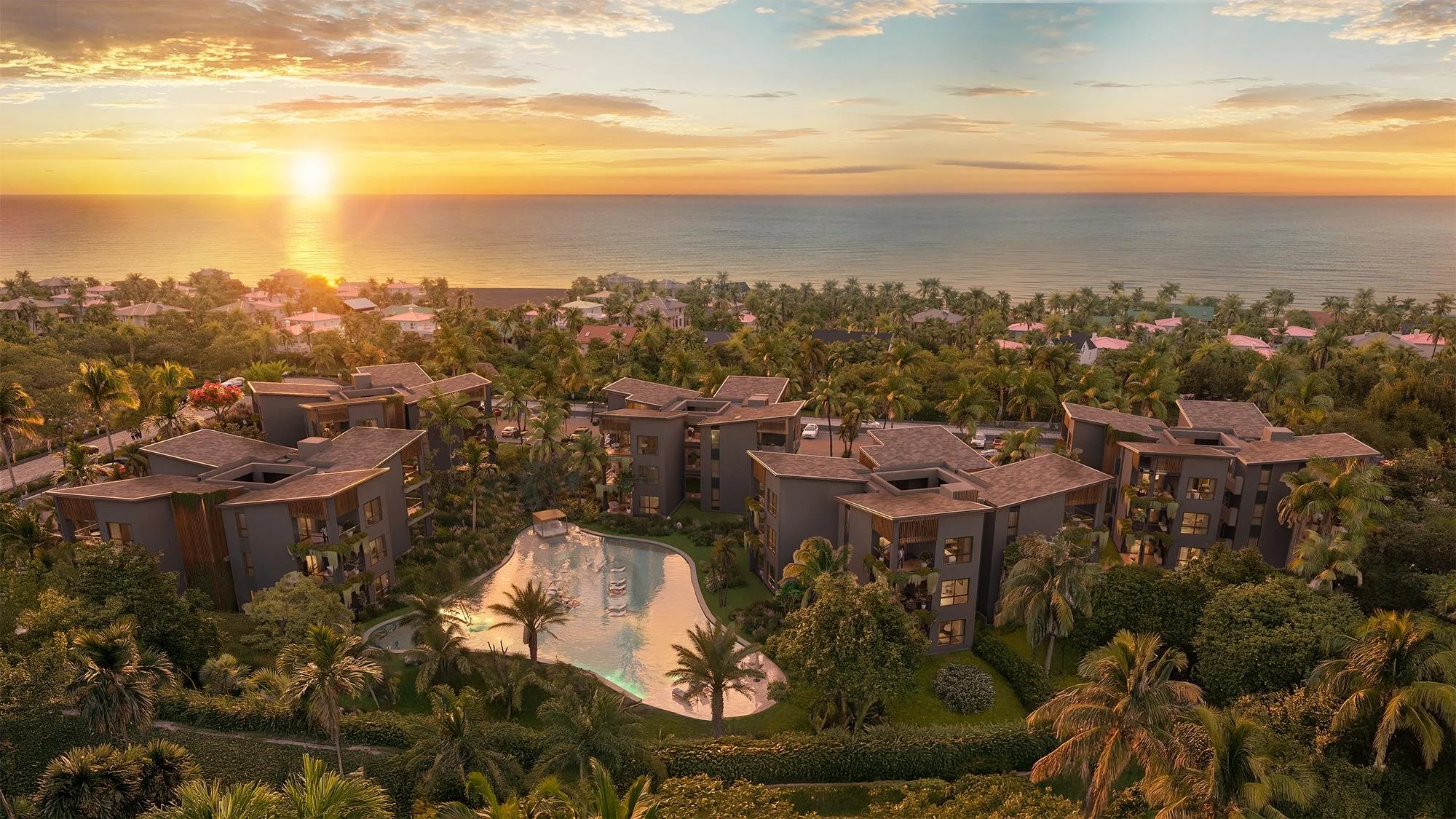 Complejo de apartamentos de lujo rodeado de palmeras y vegetación, con vista al mar y un atardecer. Hay una piscina entre los edificios y un entorno tropical exuberante.