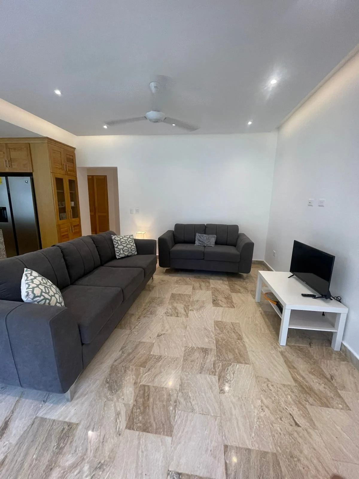 Modern living room with gray sofas, tile flooring, ceiling fan, and a small TV on a white stand.