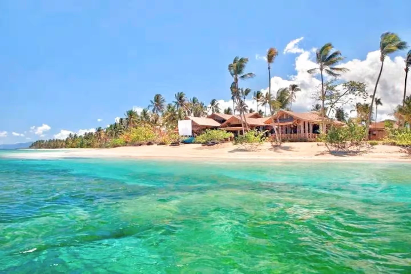 Casa en la playa con palmeras y agua cristalina en un día soleado.