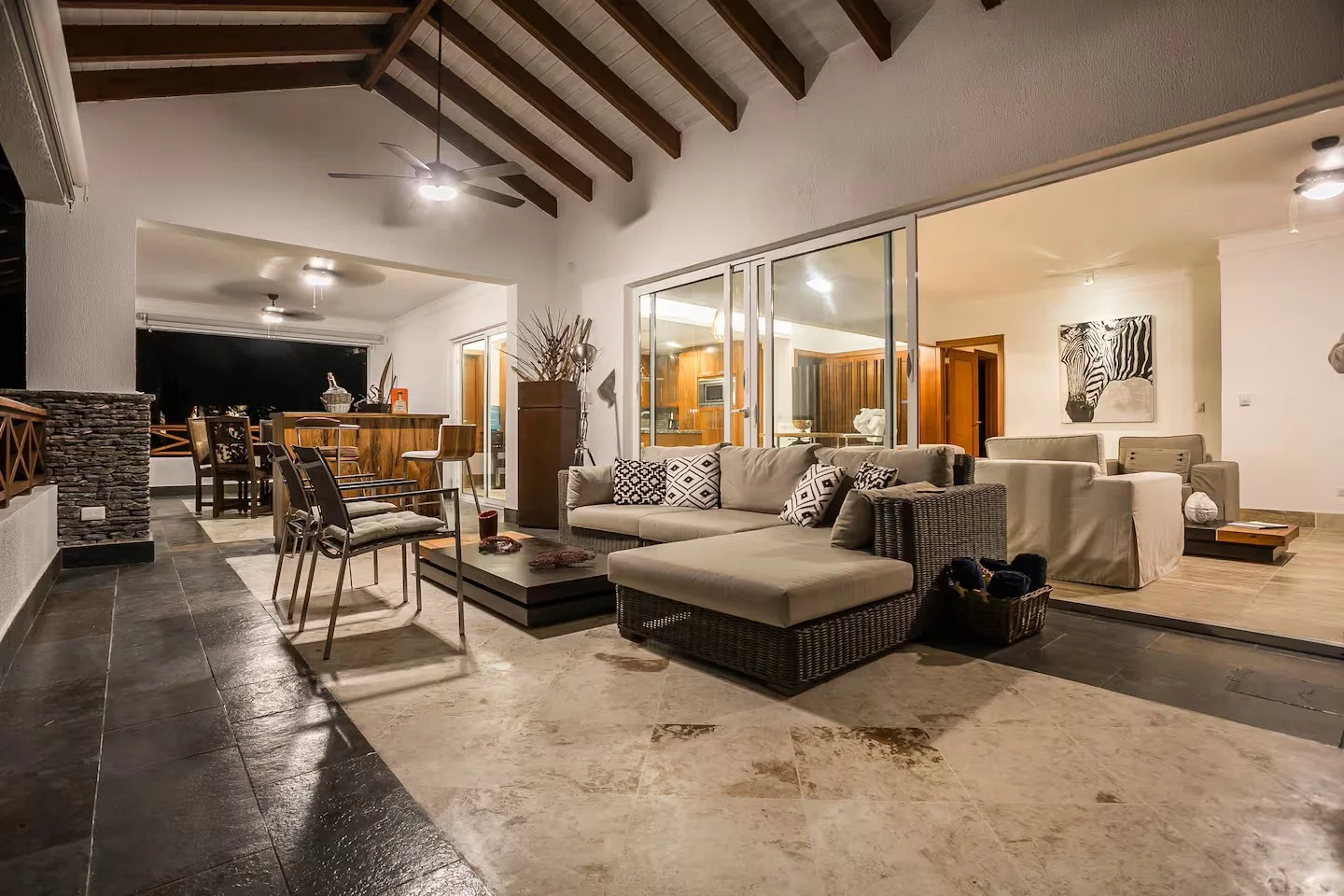 Sala de estar moderna con sofá de color beige, mesa de centro negra y sillas de comedor, iluminación cálida y decoración elegante.