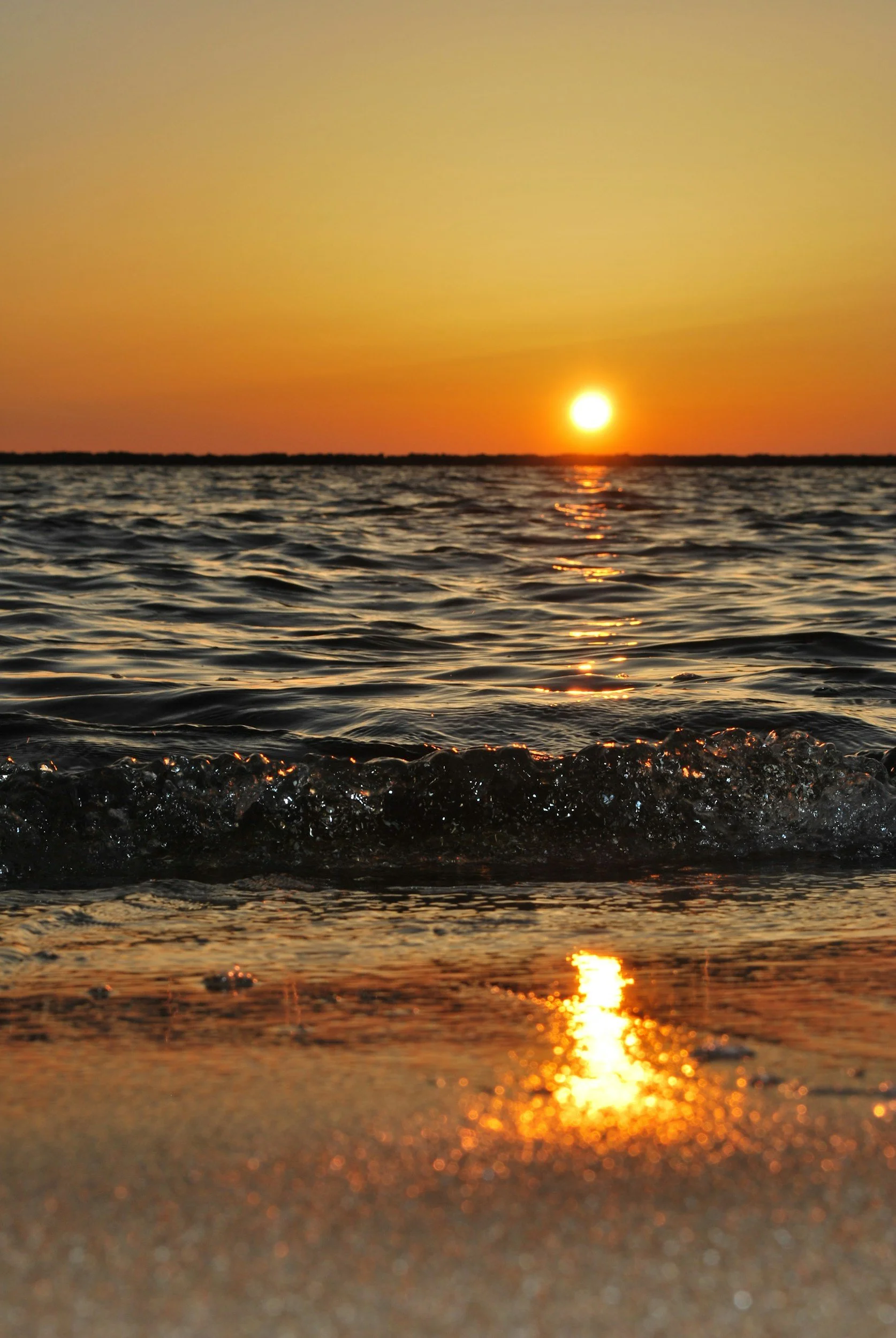 Sunset over the ocean with calm waves and a reflection on the wet sand.