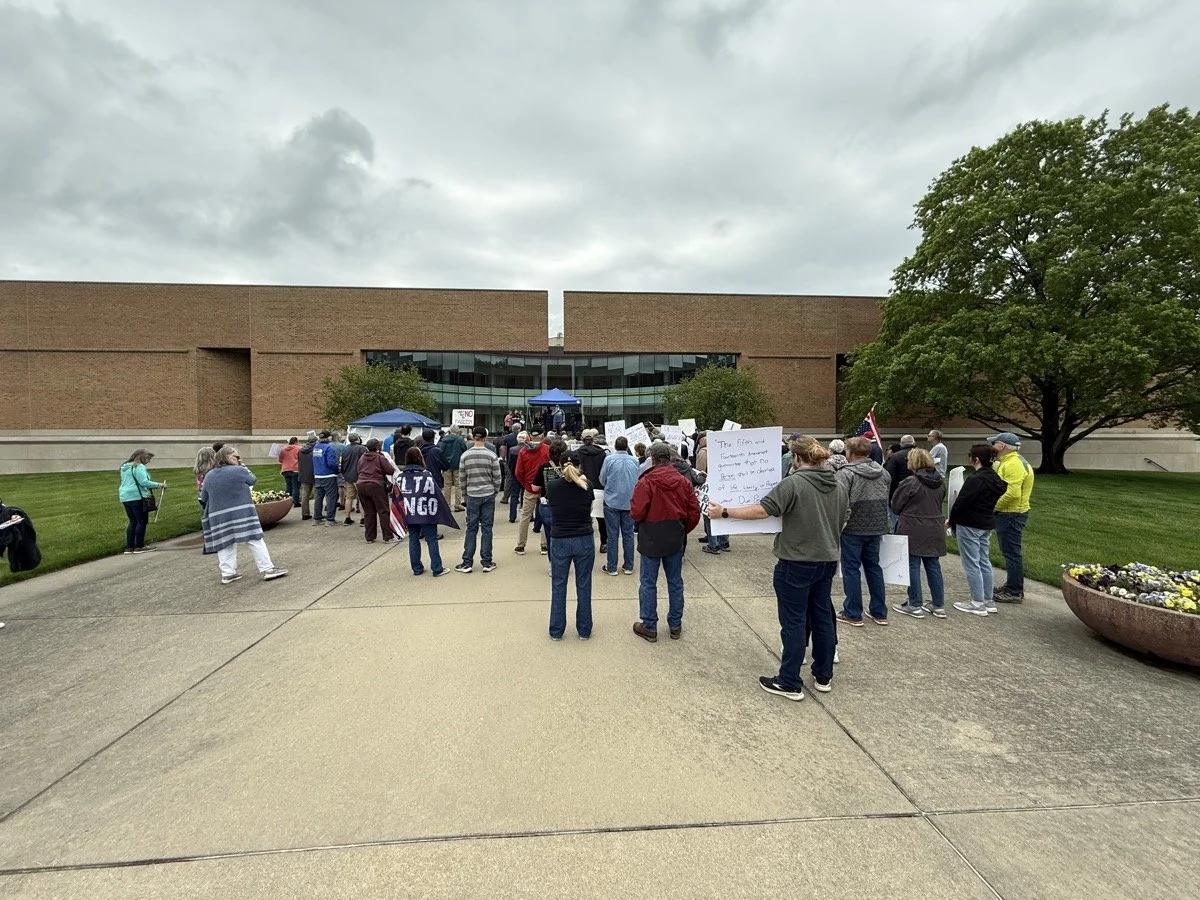People gather outside a building holding signs in a protest or rally.