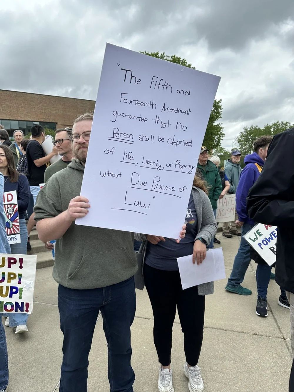 A man holding a sign with the text of the Fifth Amendment among a group of protesters.