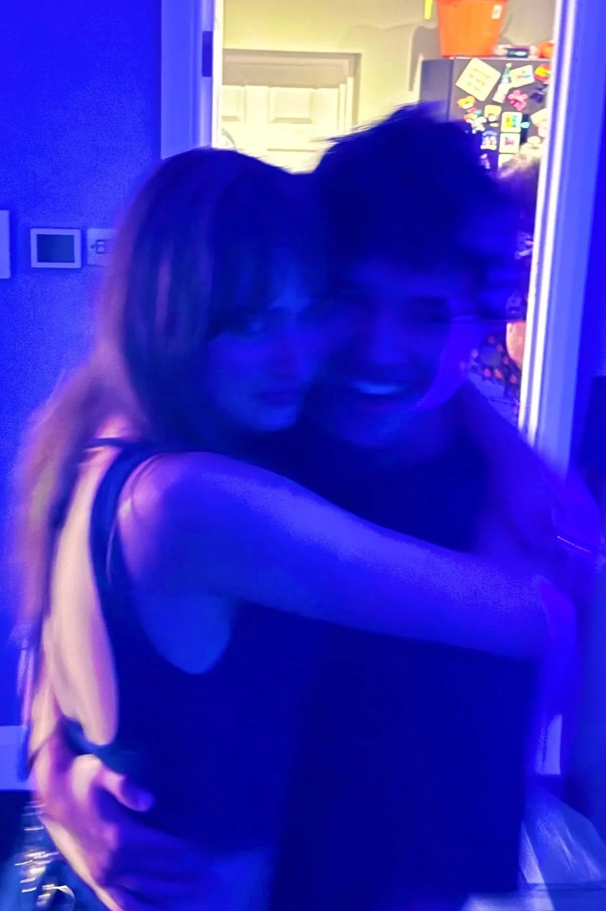 Two women hugging each other and smiling, taken in low lighting with a blue hue.