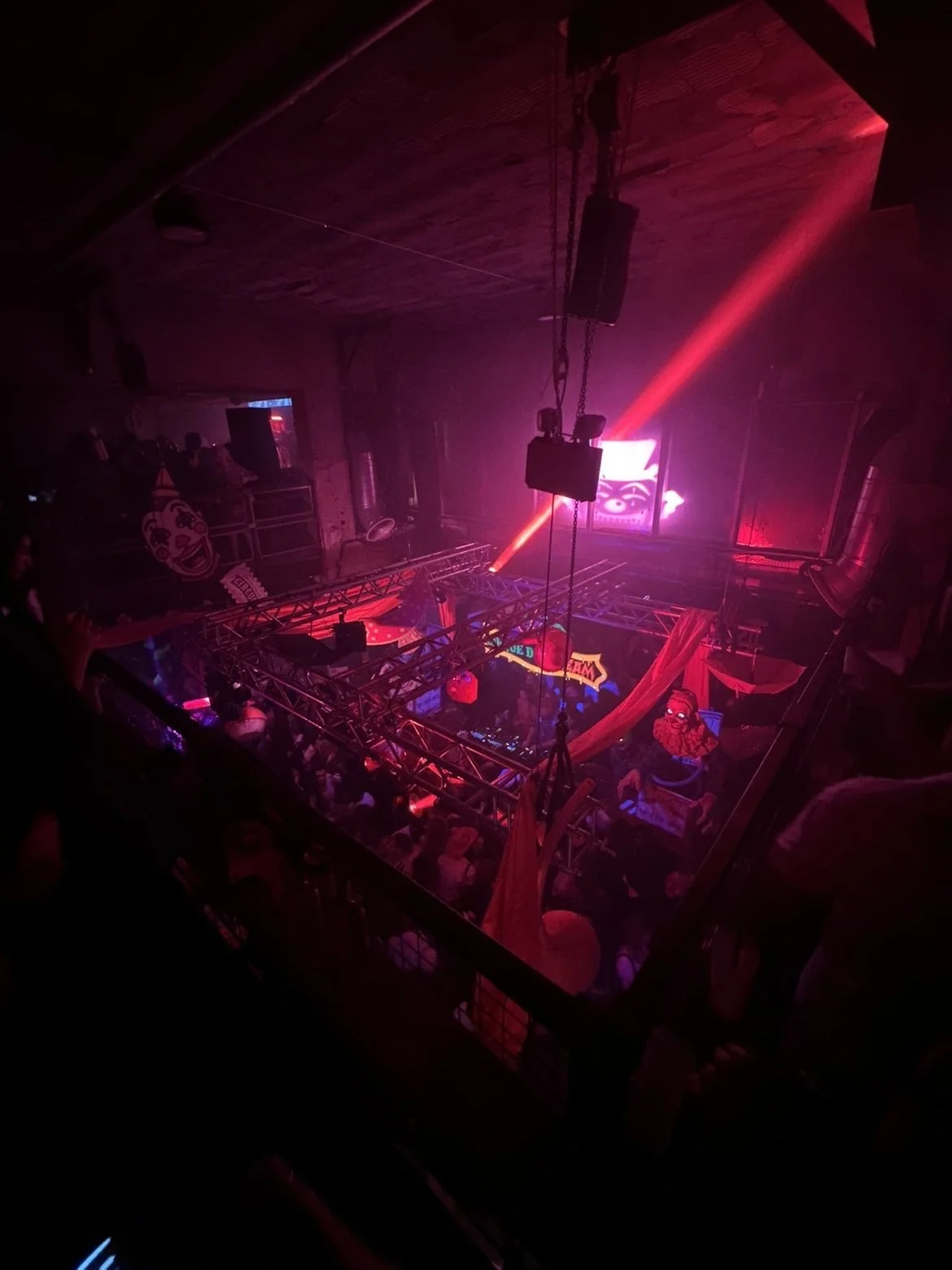 Nightclub with red and purple lighting, a dance floor, a DJ booth, and hanging decorations.