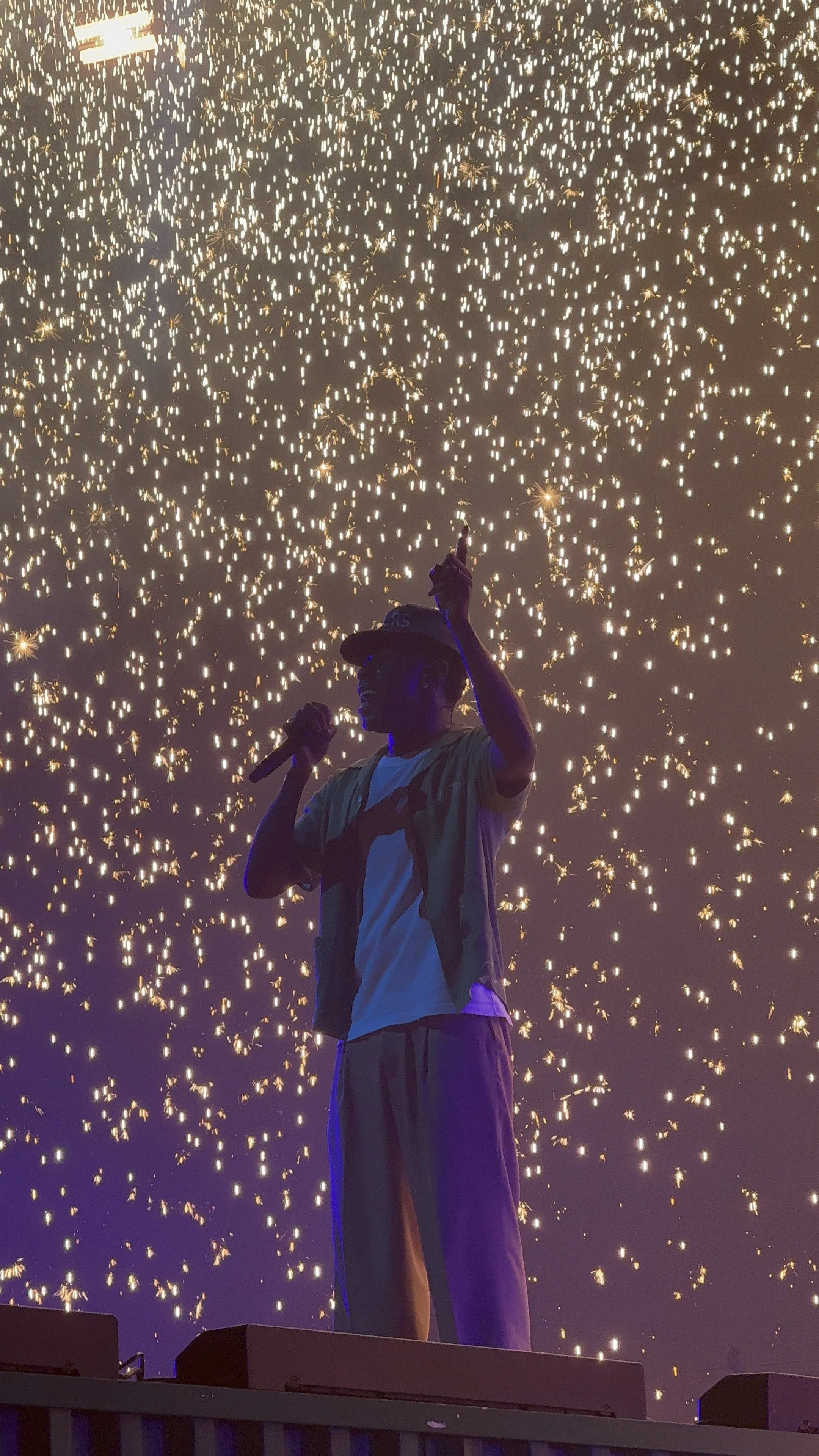 A performer with a microphone on stage with a backdrop of bright, cascading fireworks. Tyler, the Creator