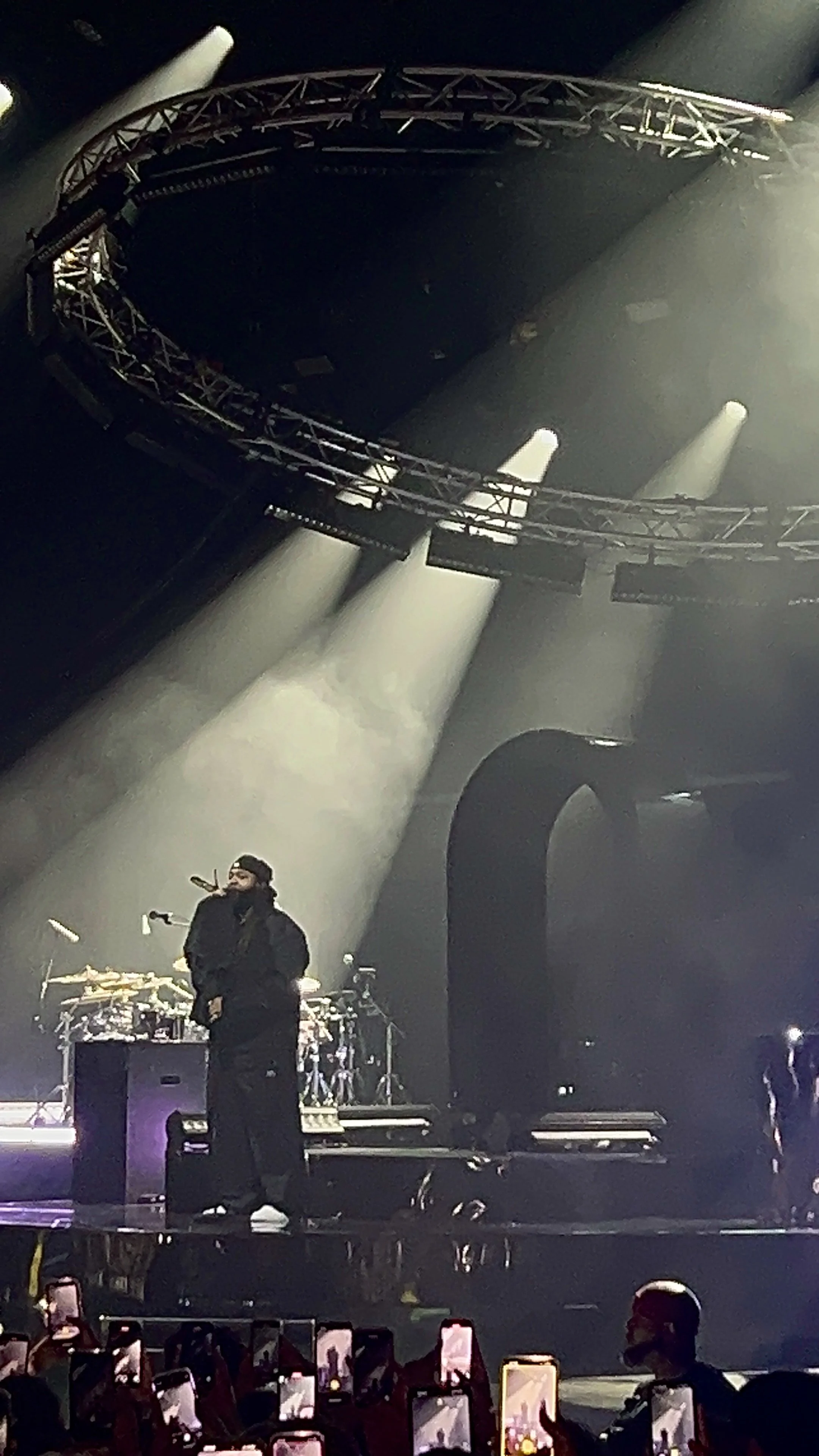 A concert stage with a performer and band, illuminated by bright stage lights, with audience members capturing the moment on their phones. PARTYNEXTDOOR O2 Academy Brixton