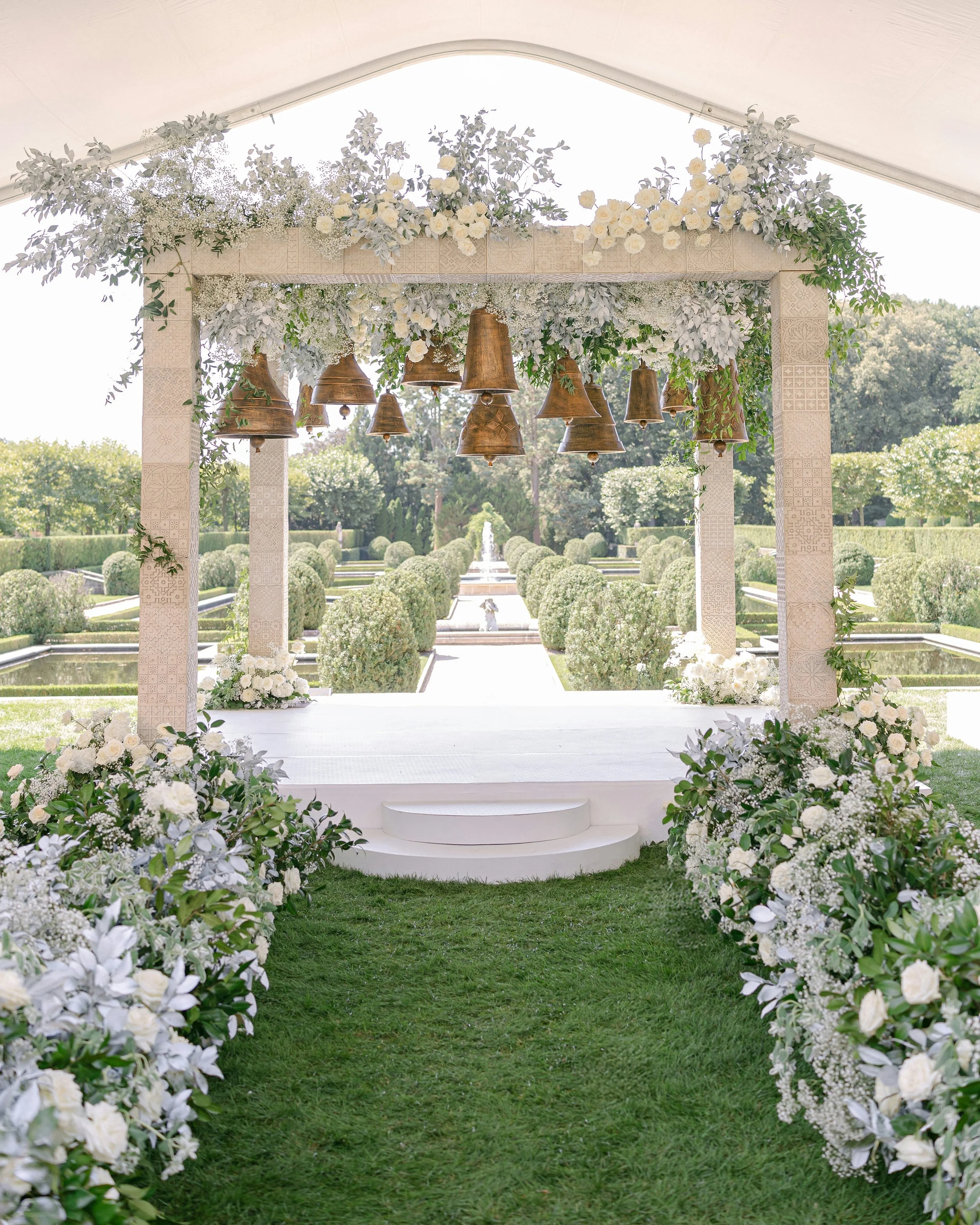 An outdoor ceremony beneath hanging brass bells at Oheka Castle
