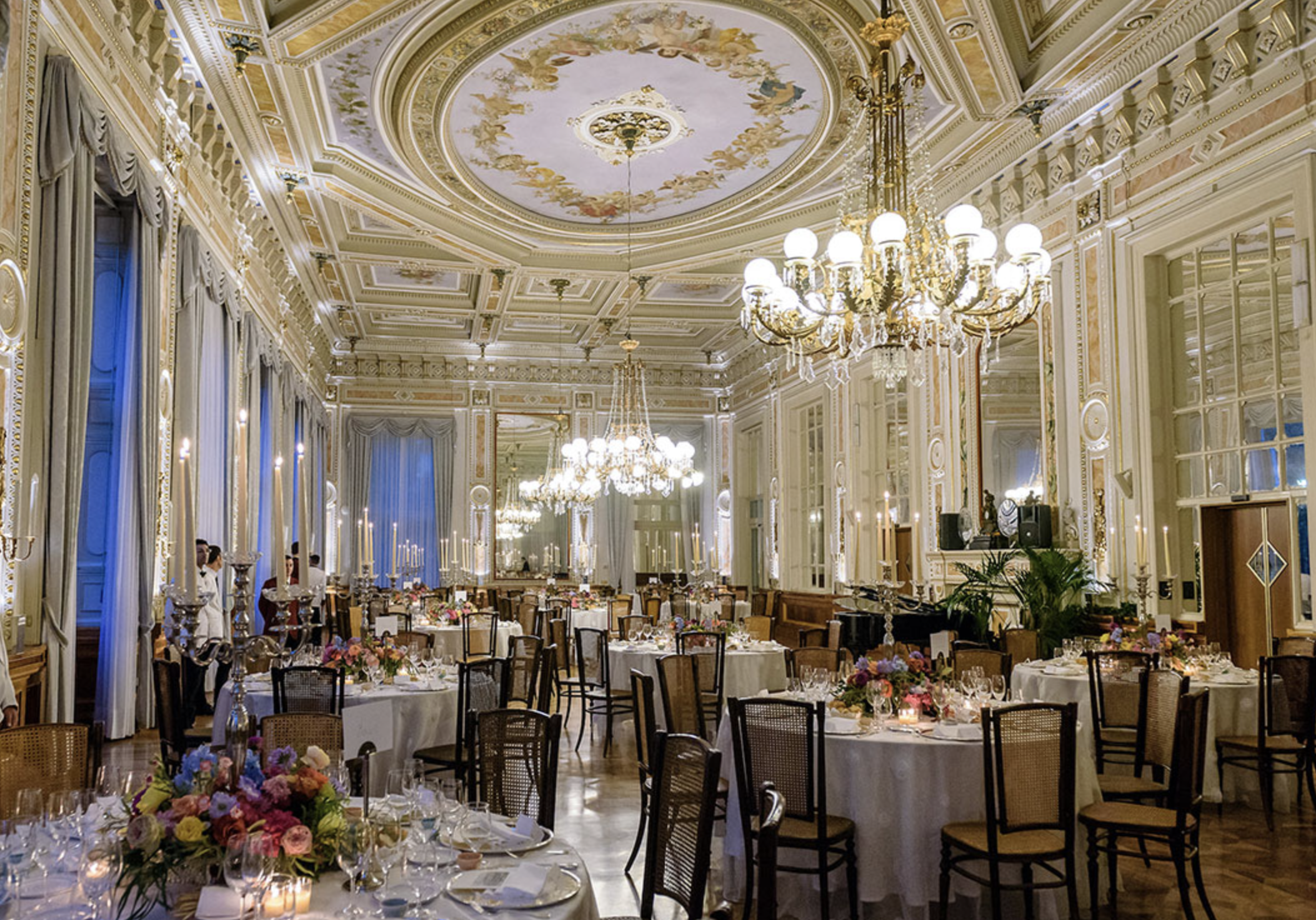 Villa Serbelloni Elegant banquet hall decorated for a formal event with chandeliers, floral centerpieces, and round tables set with glassware and candles.