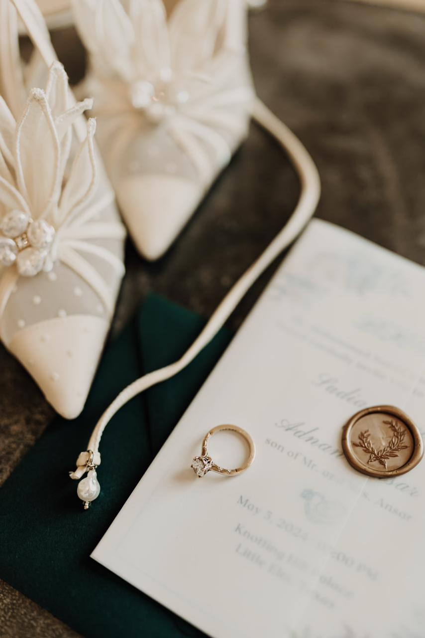 A wedding invitation with a ring, a wax seal and white decorative shoes