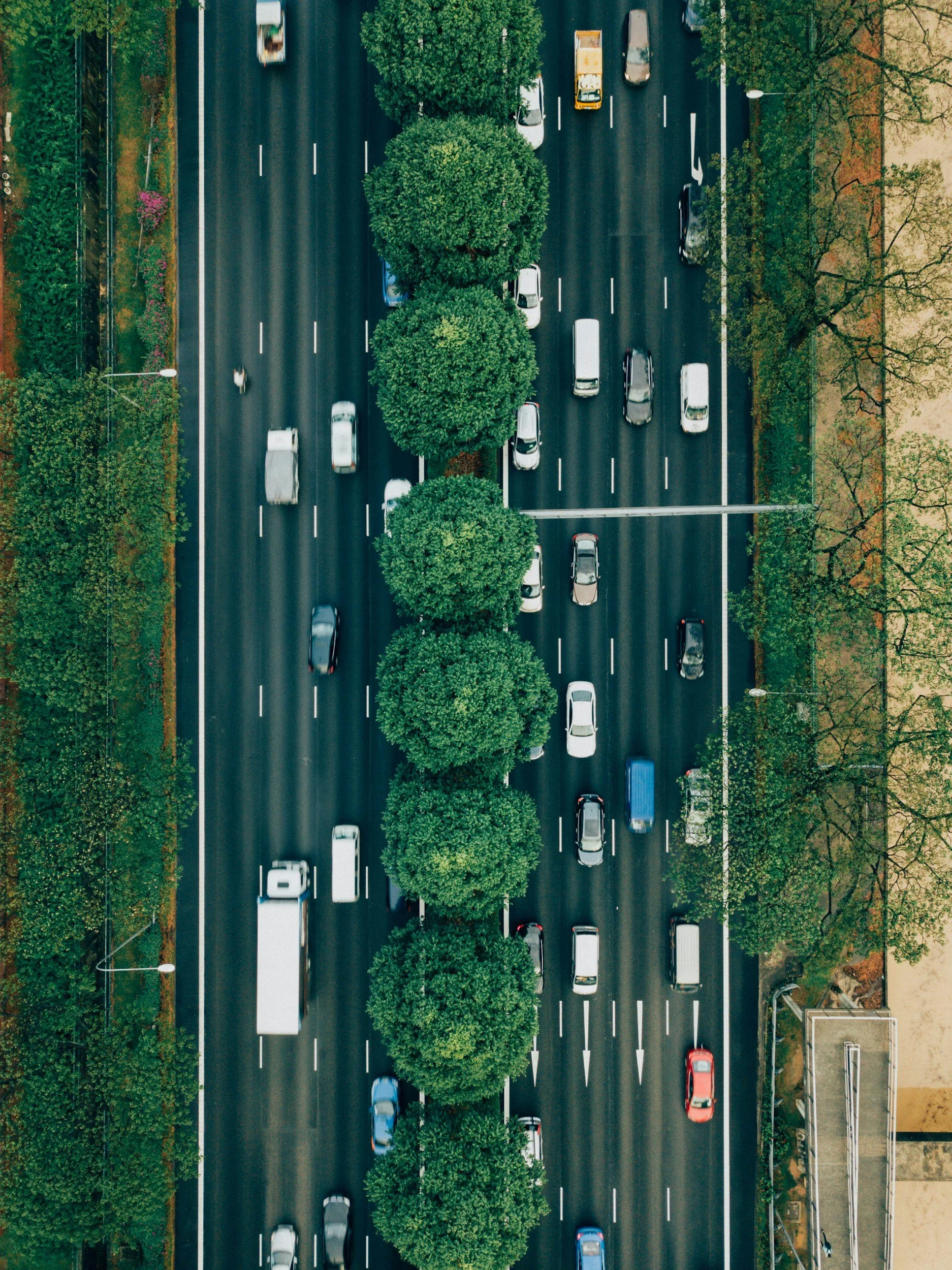 Aerial view of a multi-lane highway with cars and trucks, separated by a row of trees.
