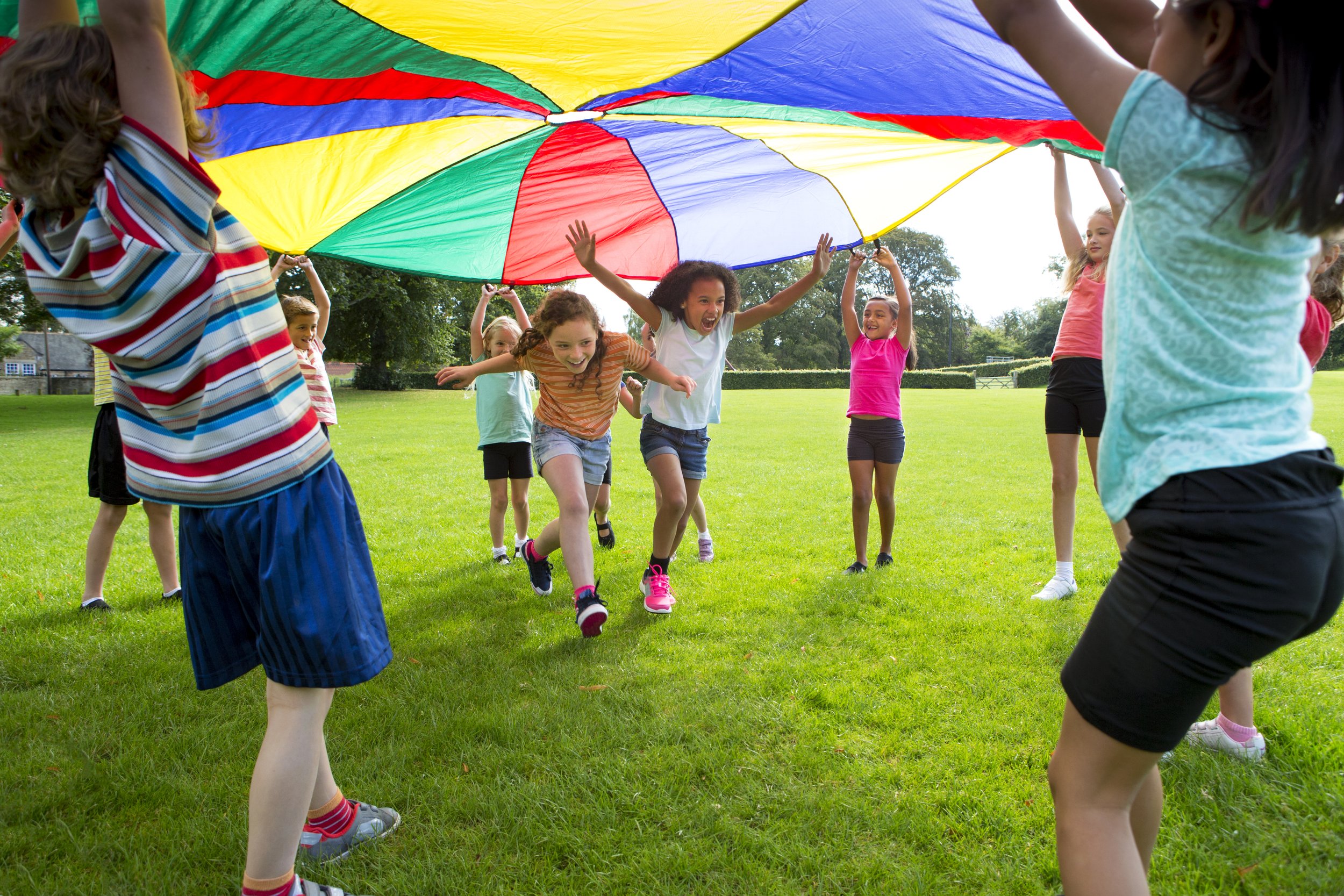 Children playing with a large, colorful parachute outdoors in a grassy park.