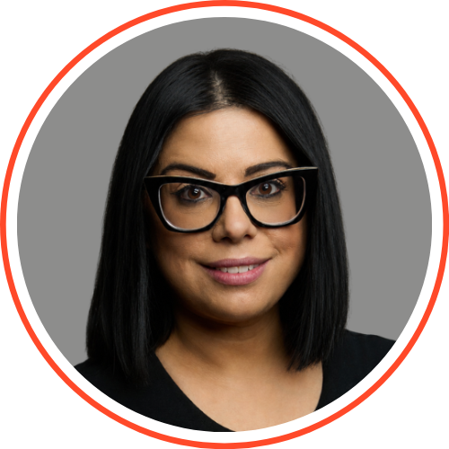 Professional headshot of a woman with long brown hair wearing black glasses and a black lace top smiles against a grey background with a red circular border.