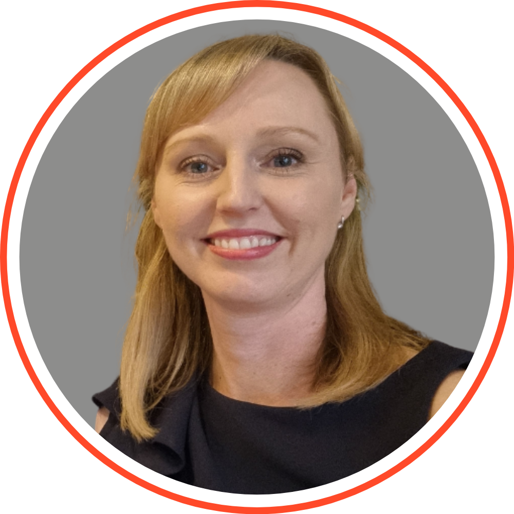 Professional headshot of a woman with short, blonde hair, wearing a black blazer and black shirt, smiling, against a grey background with a red circular border.