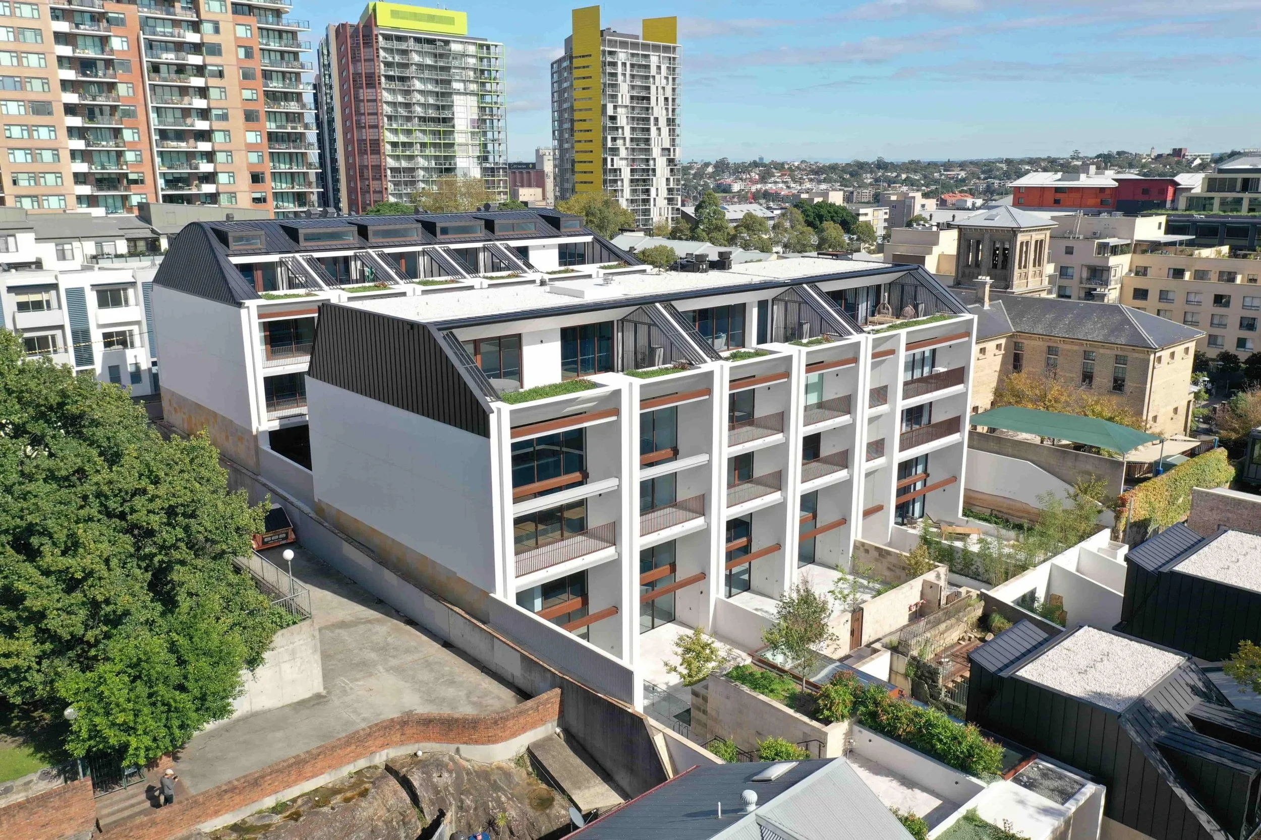 Modern multi-story residential building in an urban area with various high-rise buildings visible in the background and trees in the vicinity.