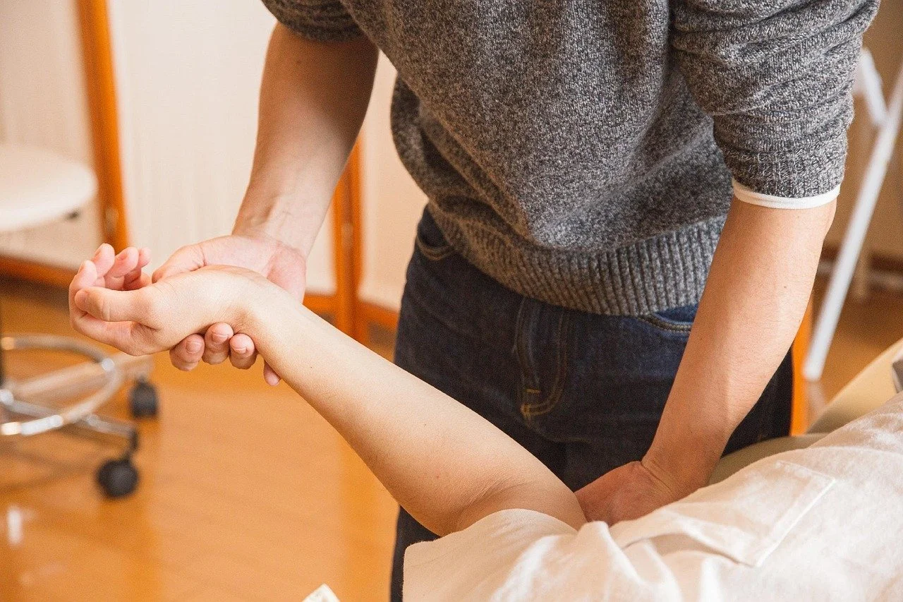 A Therapist holding the wrist of a patient lying in a hospital bed, possibly performing a medical assessment or physical therapy.