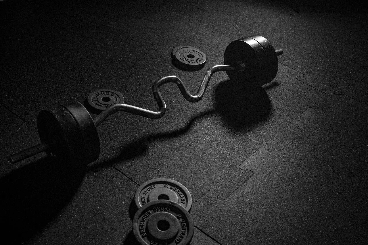 Black and white photo of an EZ curl barbell with weight plates on a gym floor.