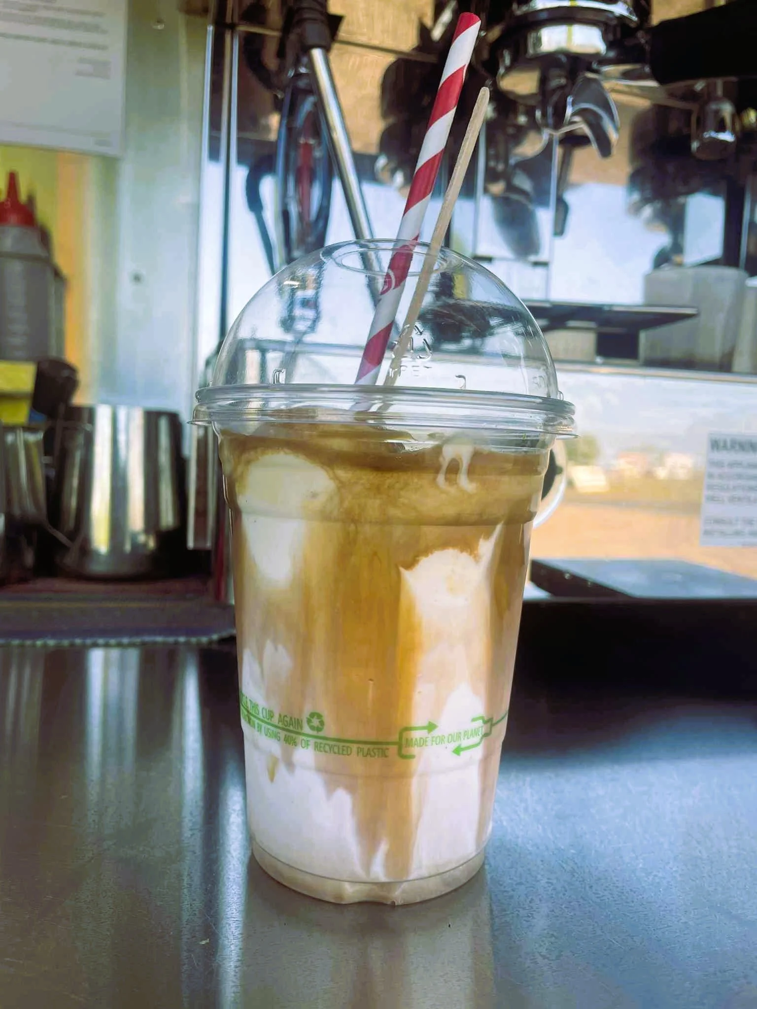 A plastic cup of iced coffee with caramel drizzle and a striped straw, sitting on a counter in a coffee shop.